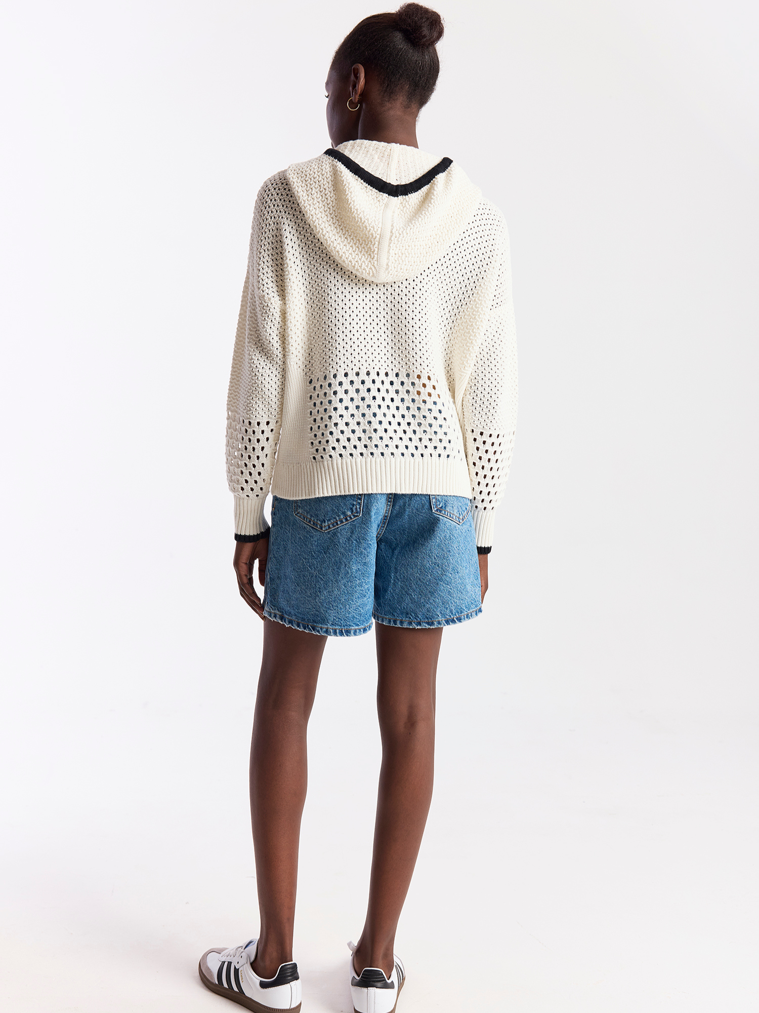 Person wearing a white perforated hoodie and denim shorts on a white background