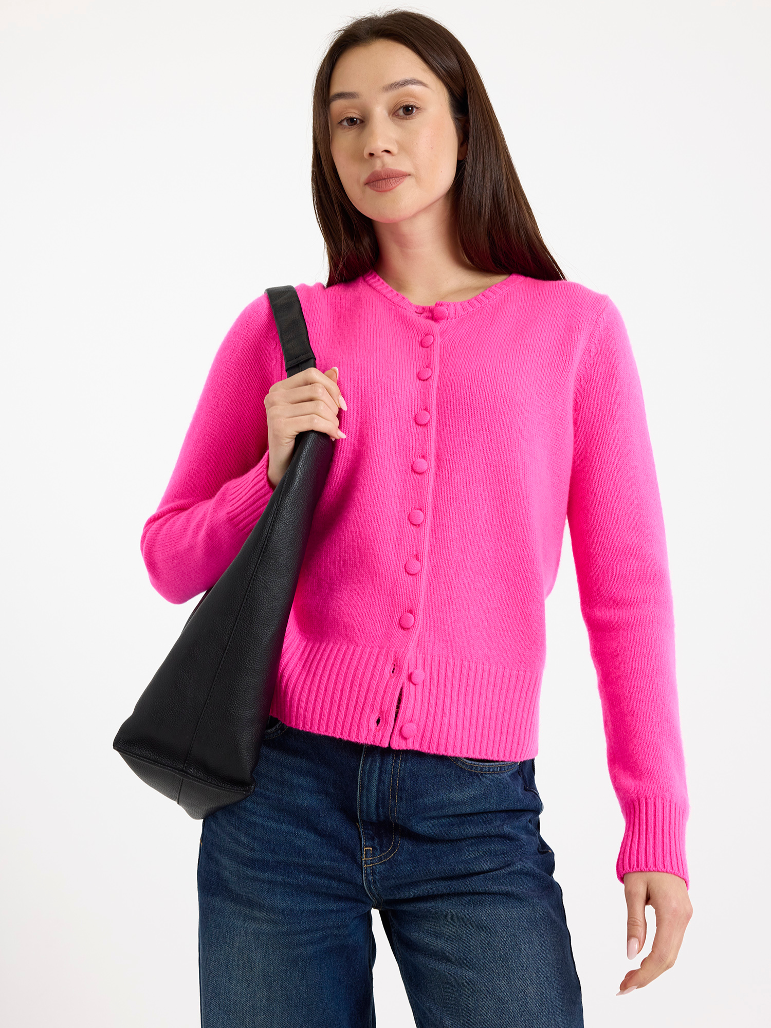 Woman wearing a bright pink cardigan holding a black bag on a white background