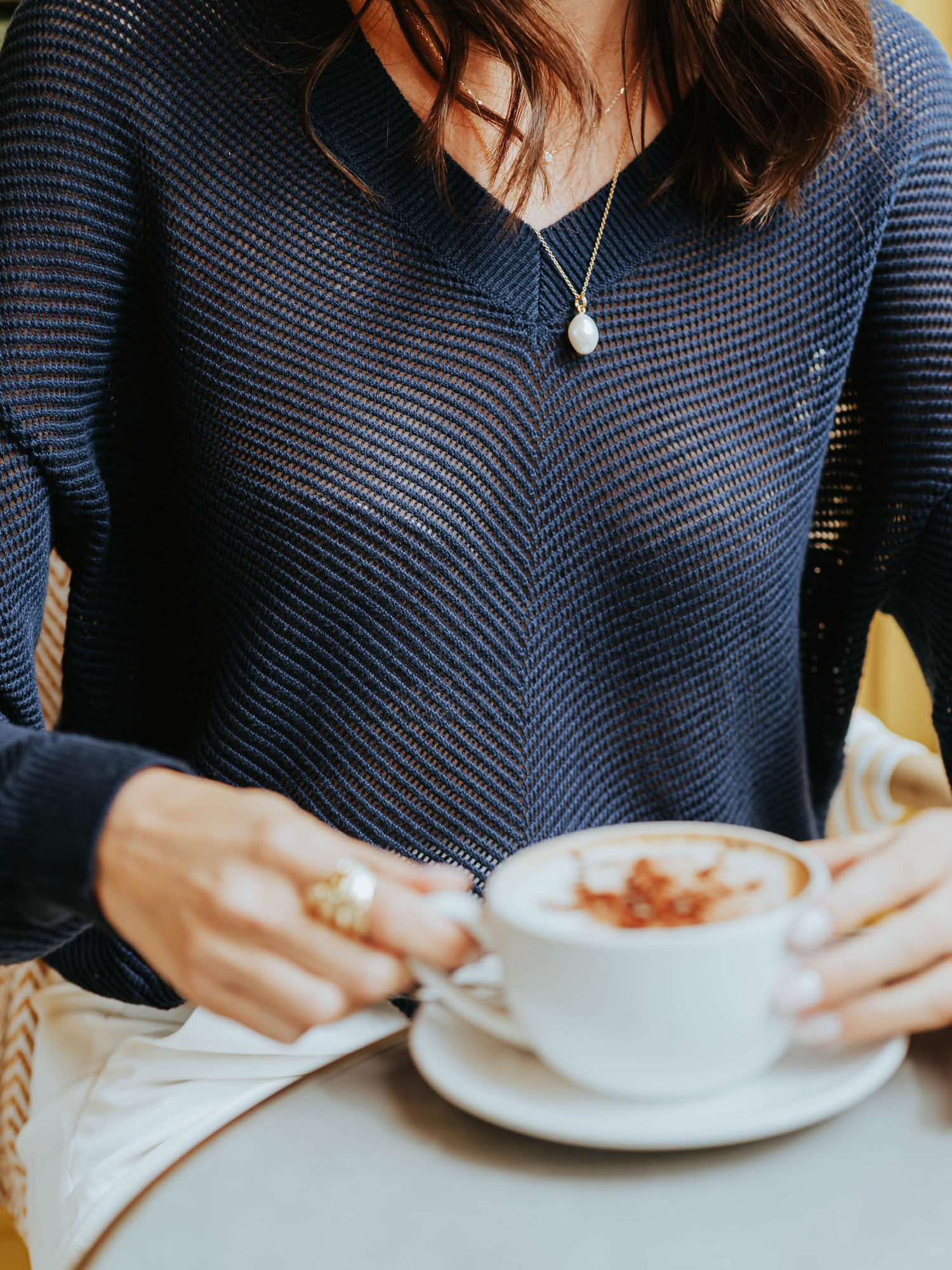 A woman wearing a navy V-neck jumper with pointelle chevron detail holding a coffee