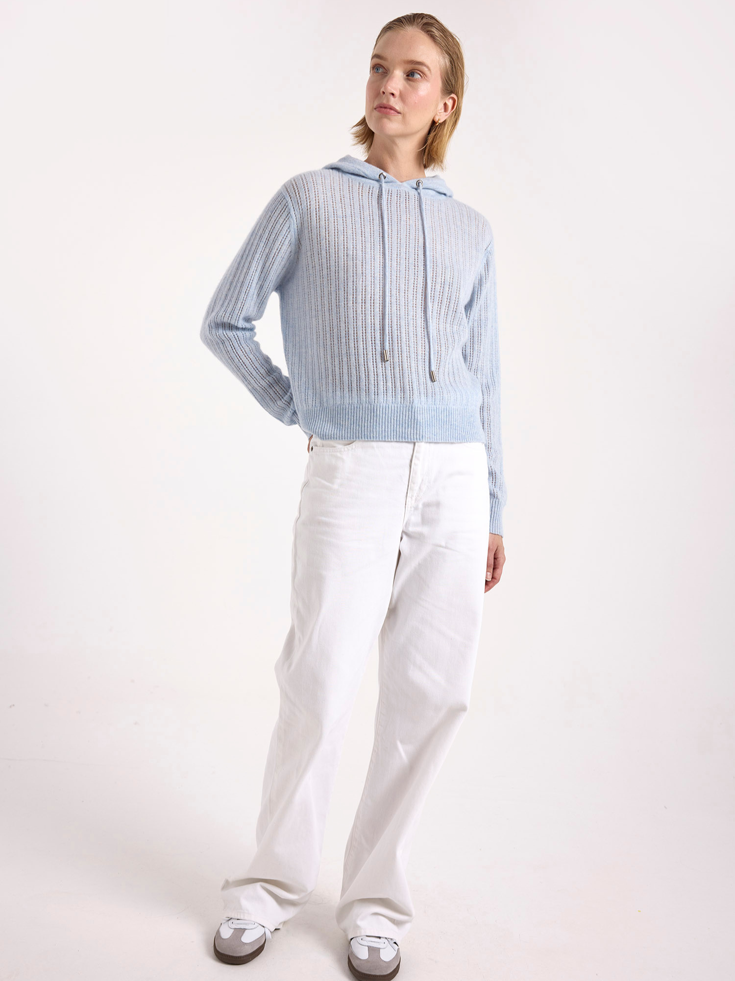 Woman wearing a light blue cashmere ribbed sweater and white pants on a white background