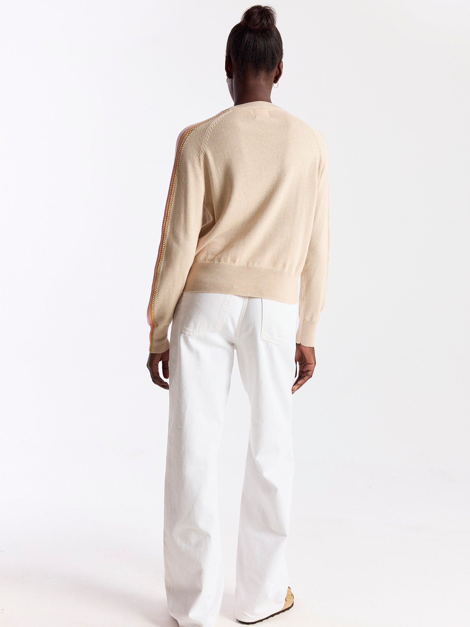Person wearing a beige sweater and white pants on a white background