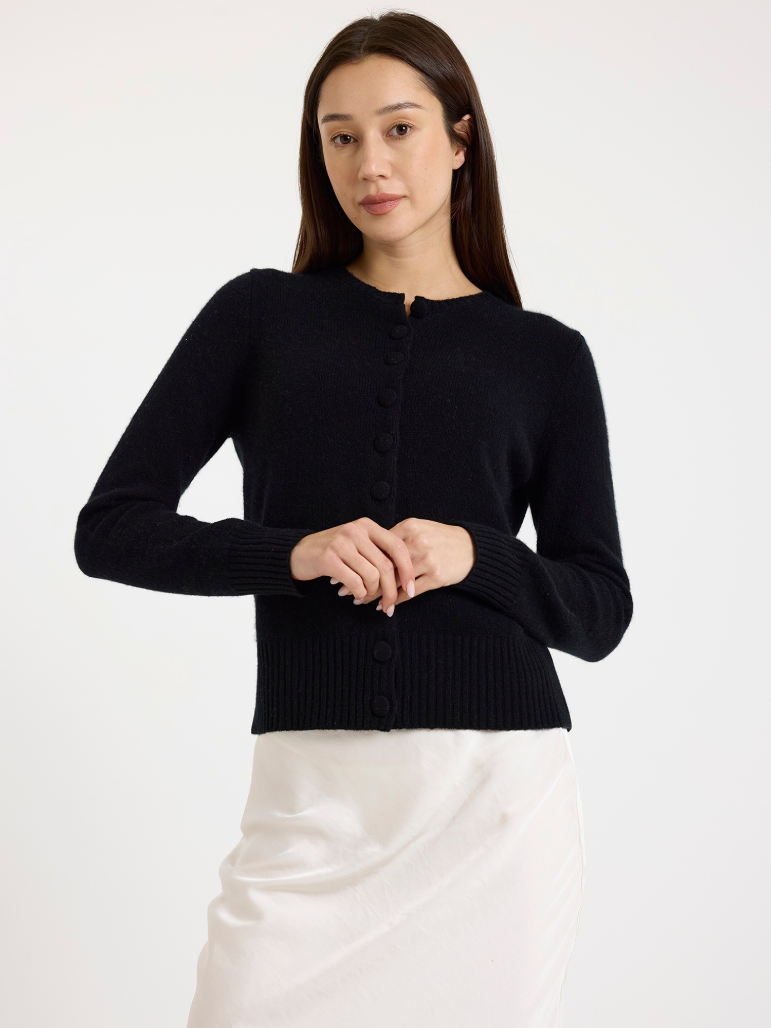 Woman wearing a black cardigan over a white skirt on a white background