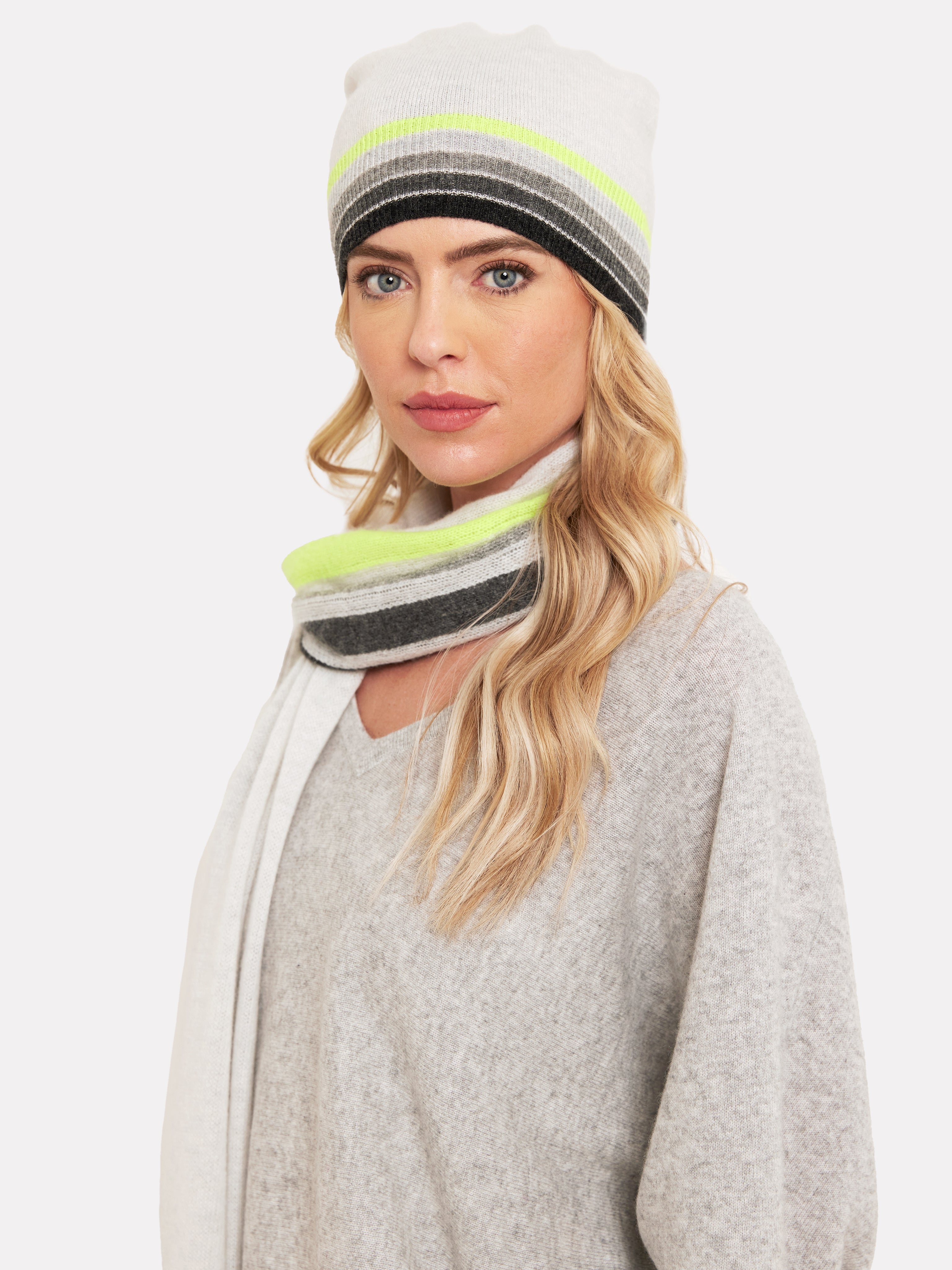 Woman wearing a light grey hat with rainbow grey and yellow colour trim and matching scarf