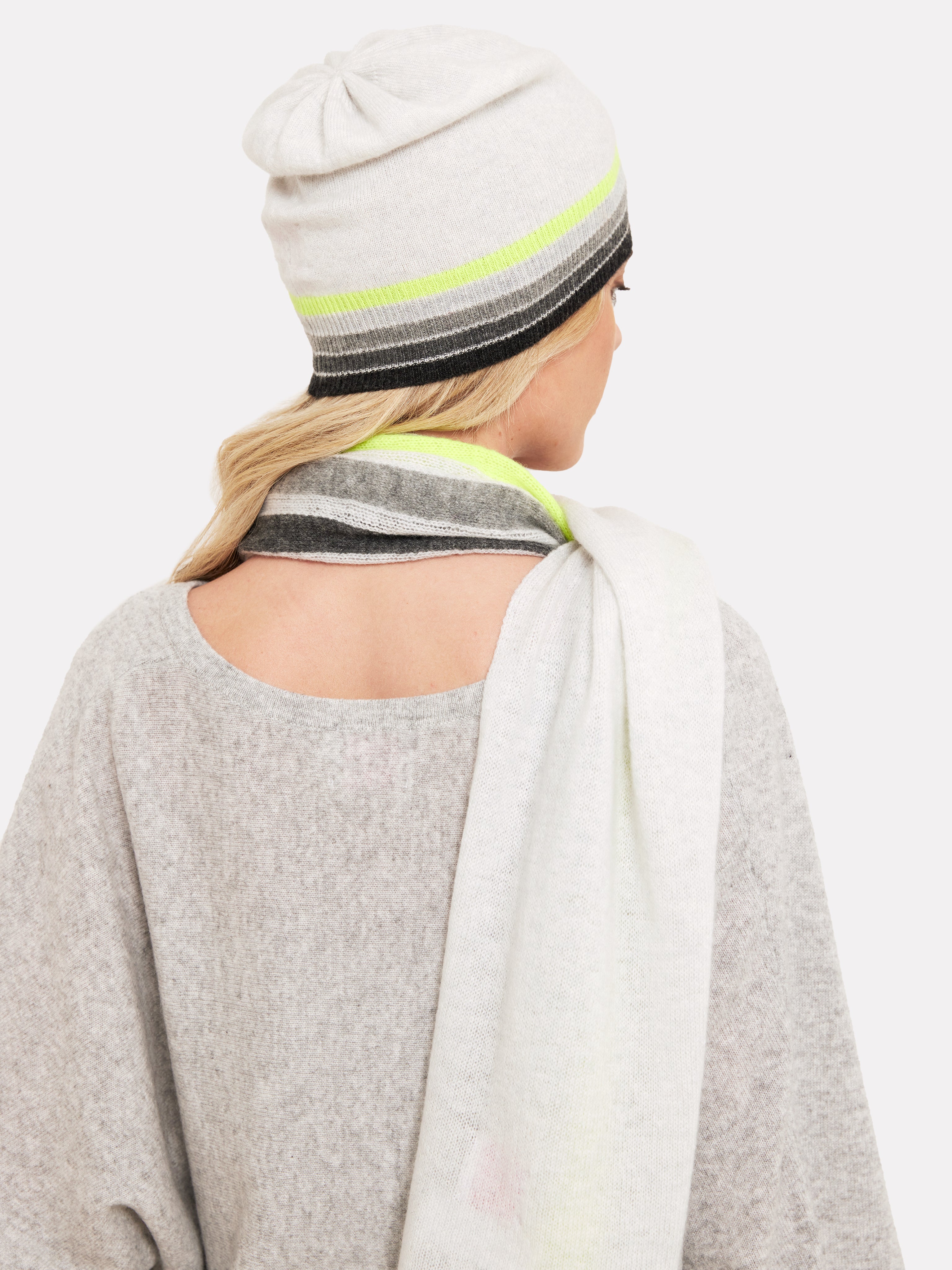 Woman wearing a light grey hat with rainbow grey and yellow colour trim and matching scarf