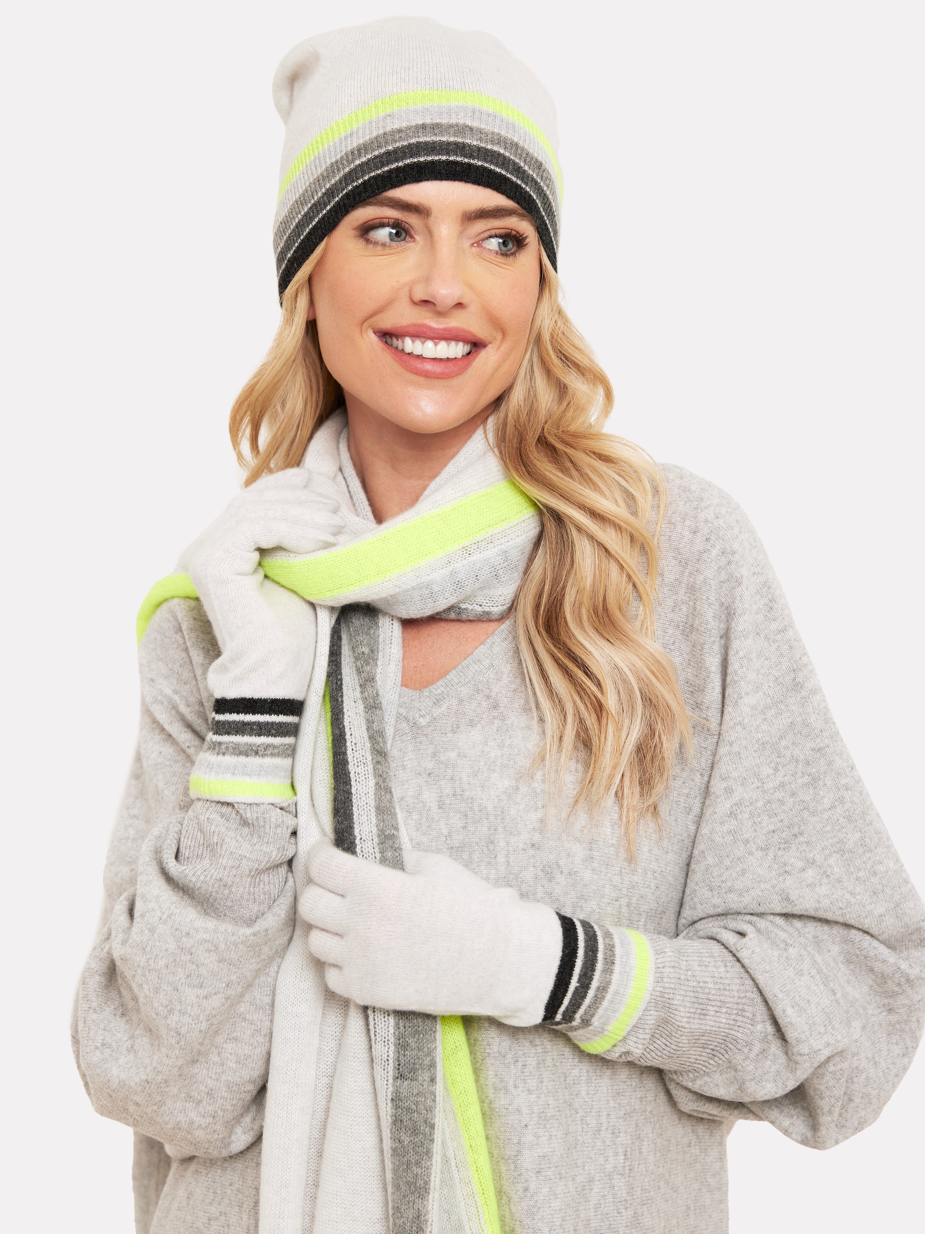 Woman wearing a light grey hat with grey and yellow rainbow trim with matching gloves and scarf