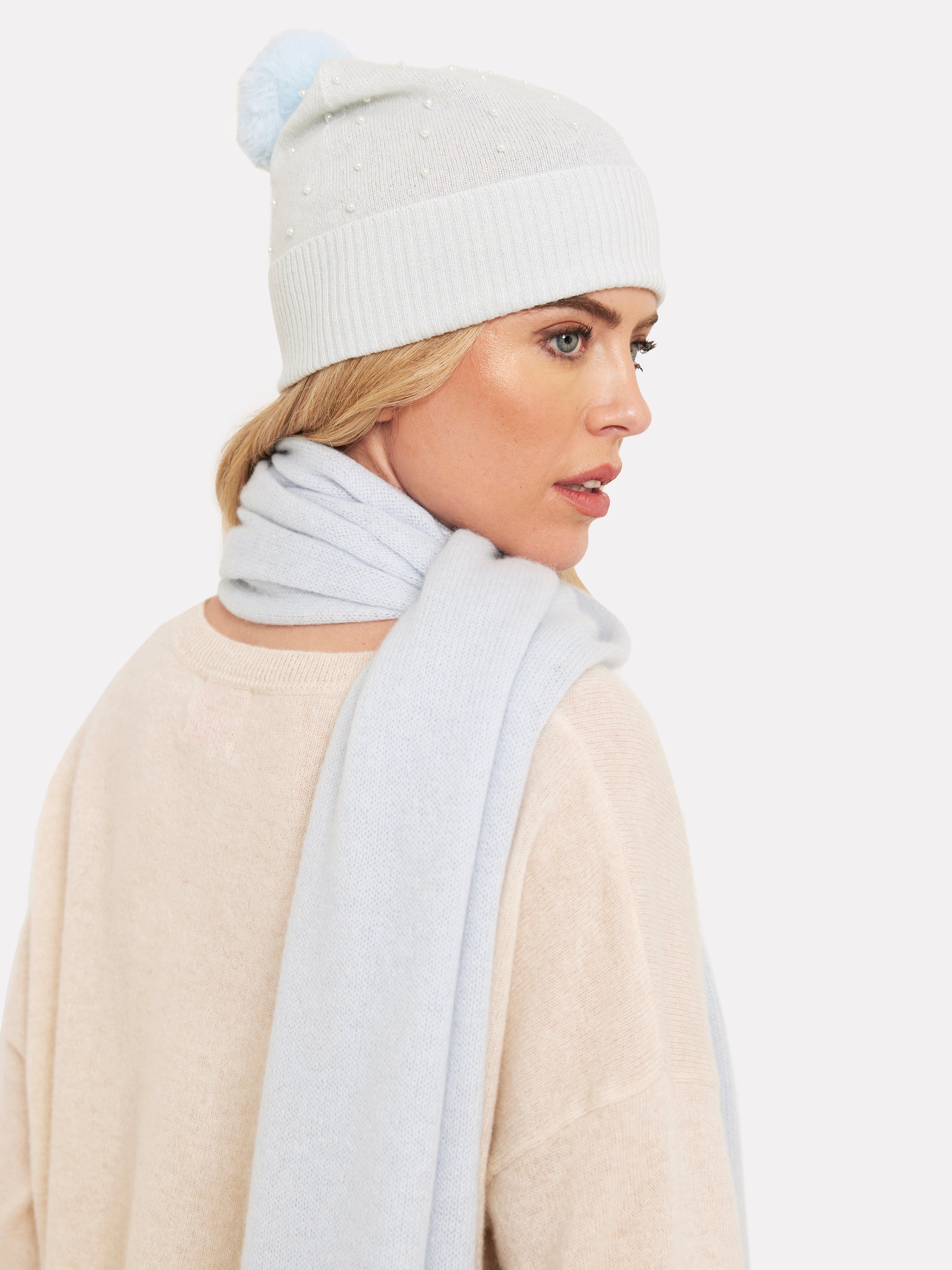 Women wearing a pale blue bobble hat with pearl detail and matching pale blue scarf