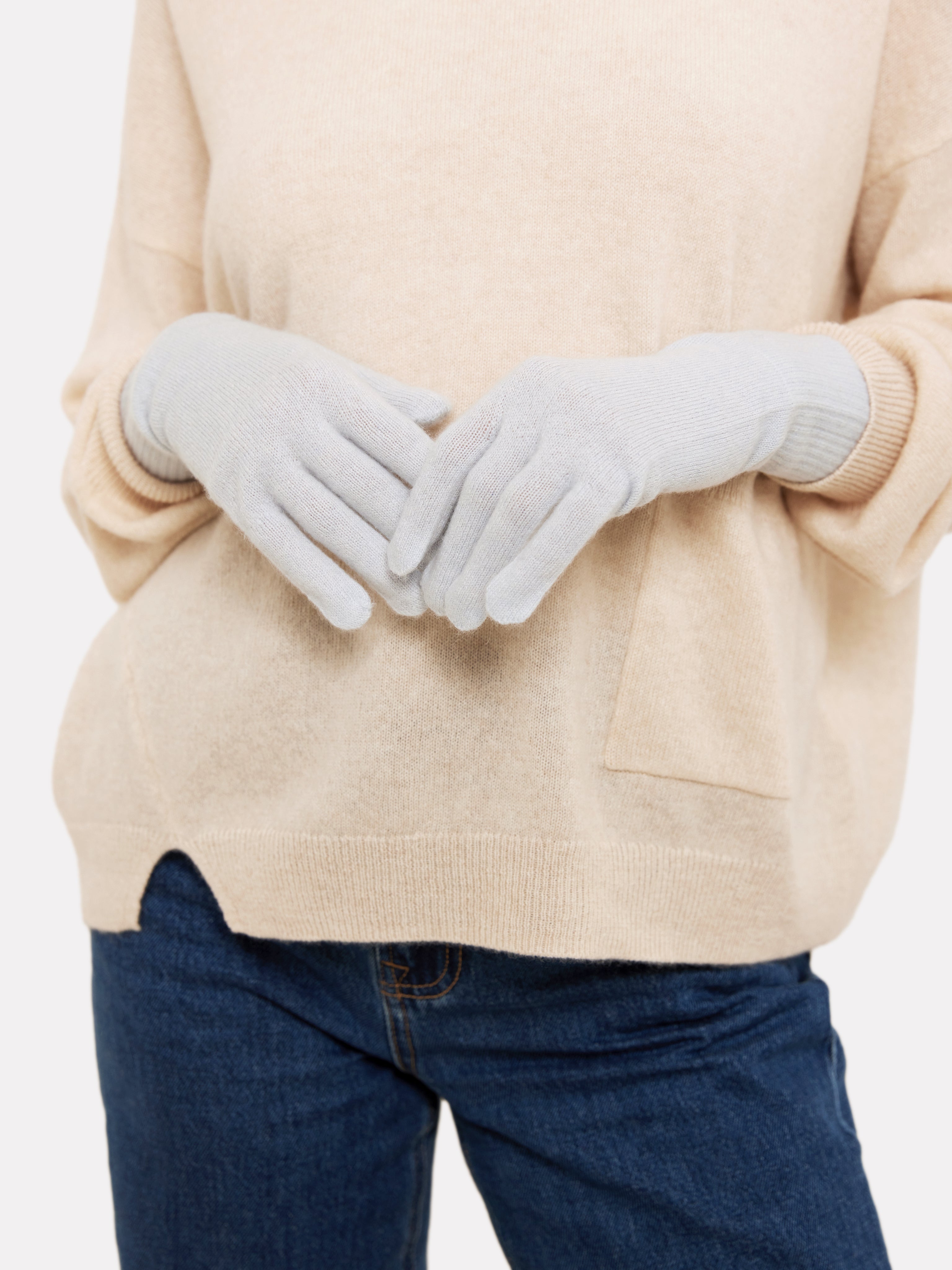 Person wearing light blue gloves with a beige sweater and blue jeans on a white background