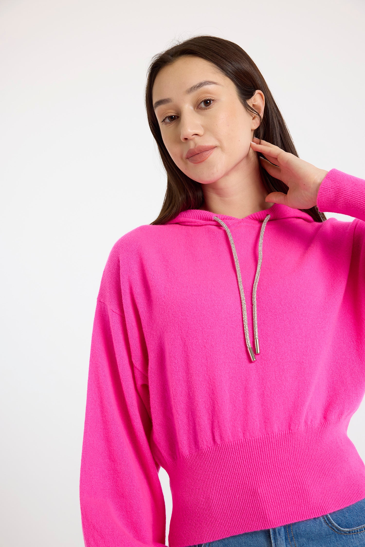 A woman wearing a pink cashmere hoodie with rhinestone drawstrings, over a white background.