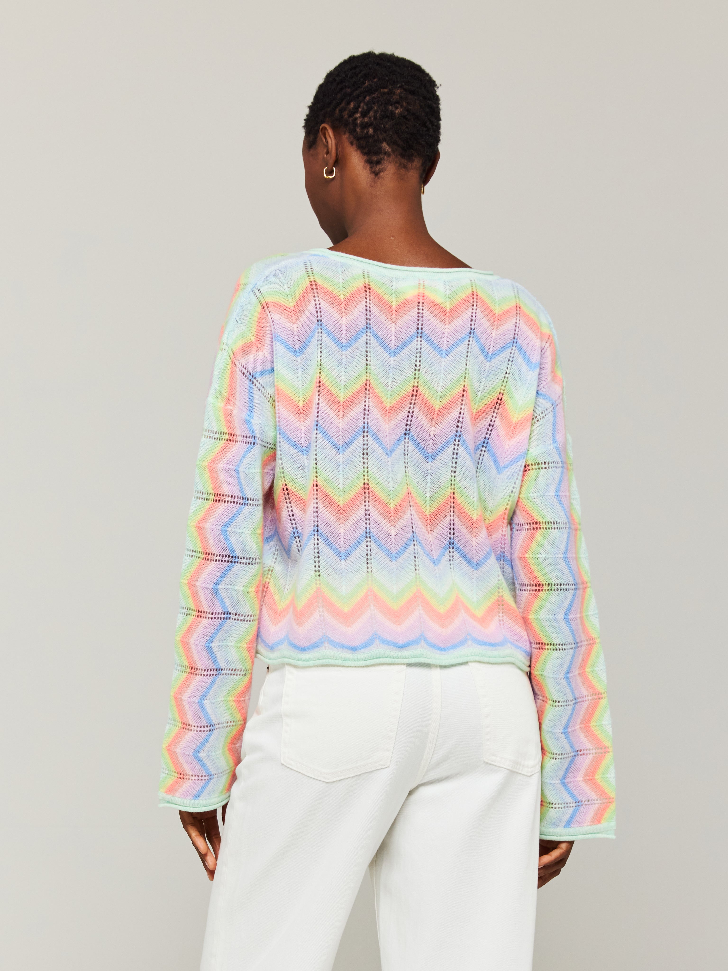 A person wearing an oversized multicolored cashmere sweater with a slash neck, paired with white trousers.