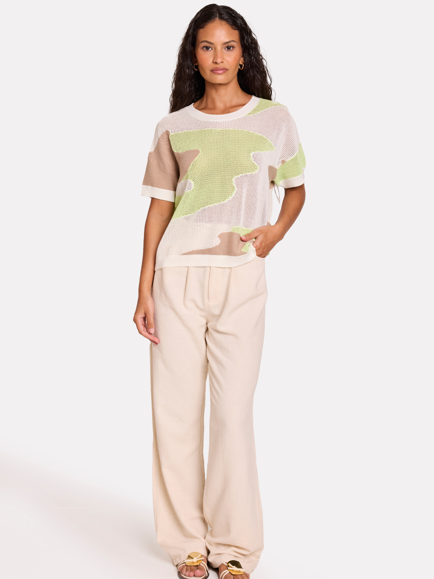 Woman wearing a beige and green camo patterned top with beige pants on a white background