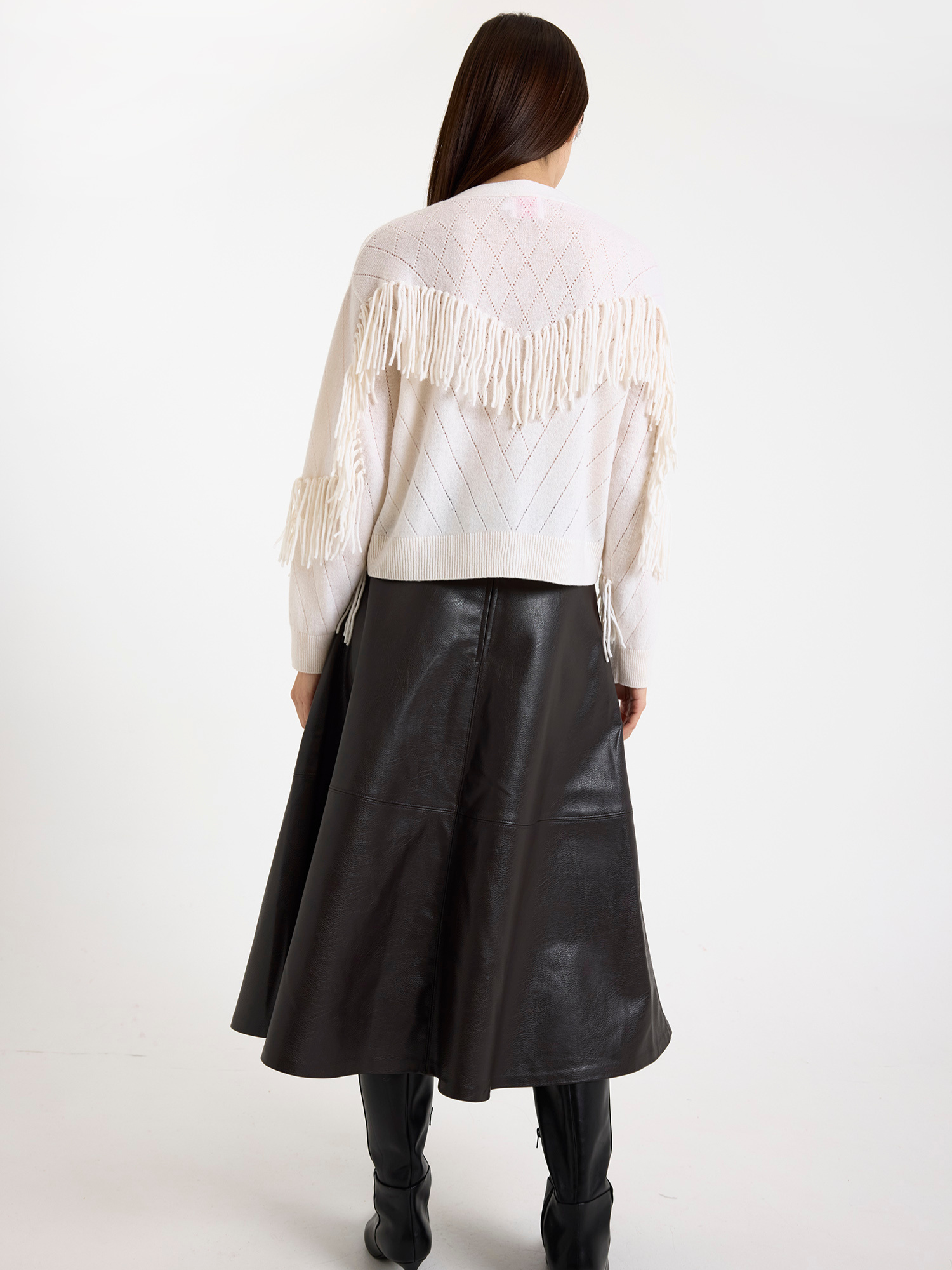 Woman wearing a white fringed cardigan with a brown leather skirt on a white background