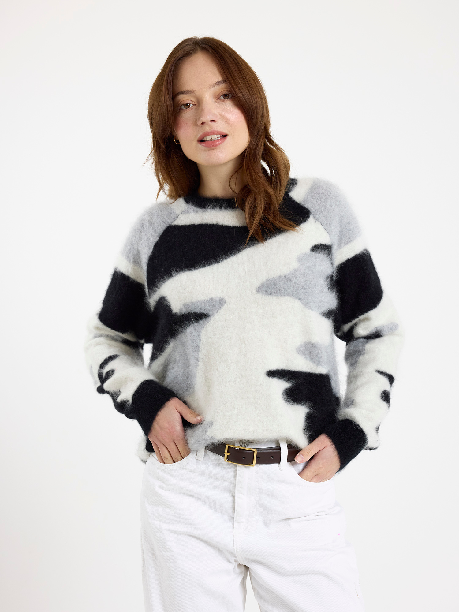 Woman wearing a black, white and grey camo patterned sweater with white jeans on a white background