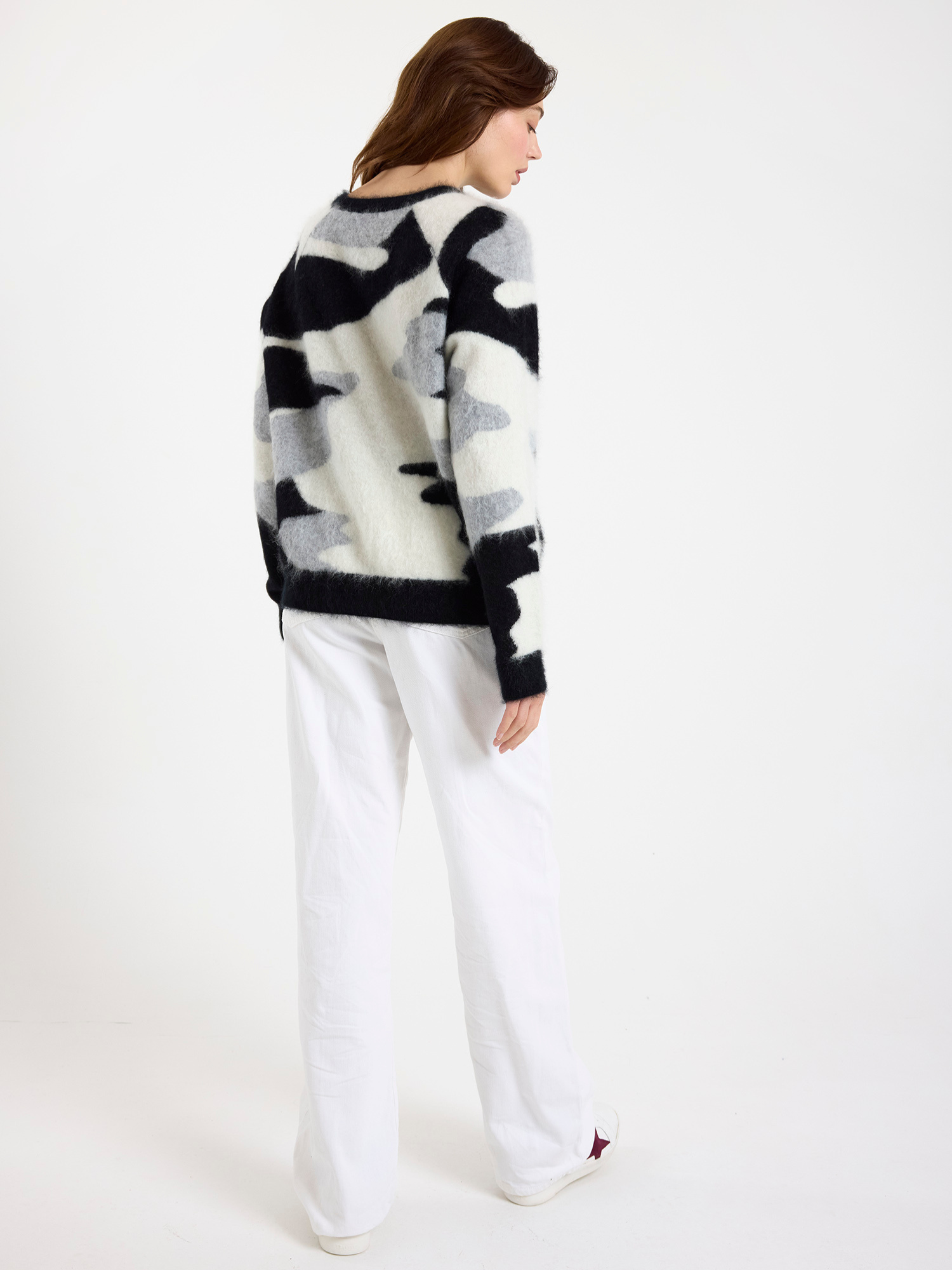 Woman wearing a black, white and grey camo patterned sweater with white jeans on a white background