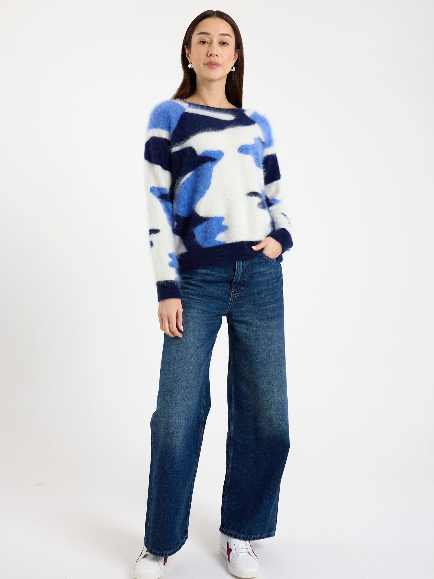Woman wearing a blue and white camo patterned sweater and blue jeans on a white background