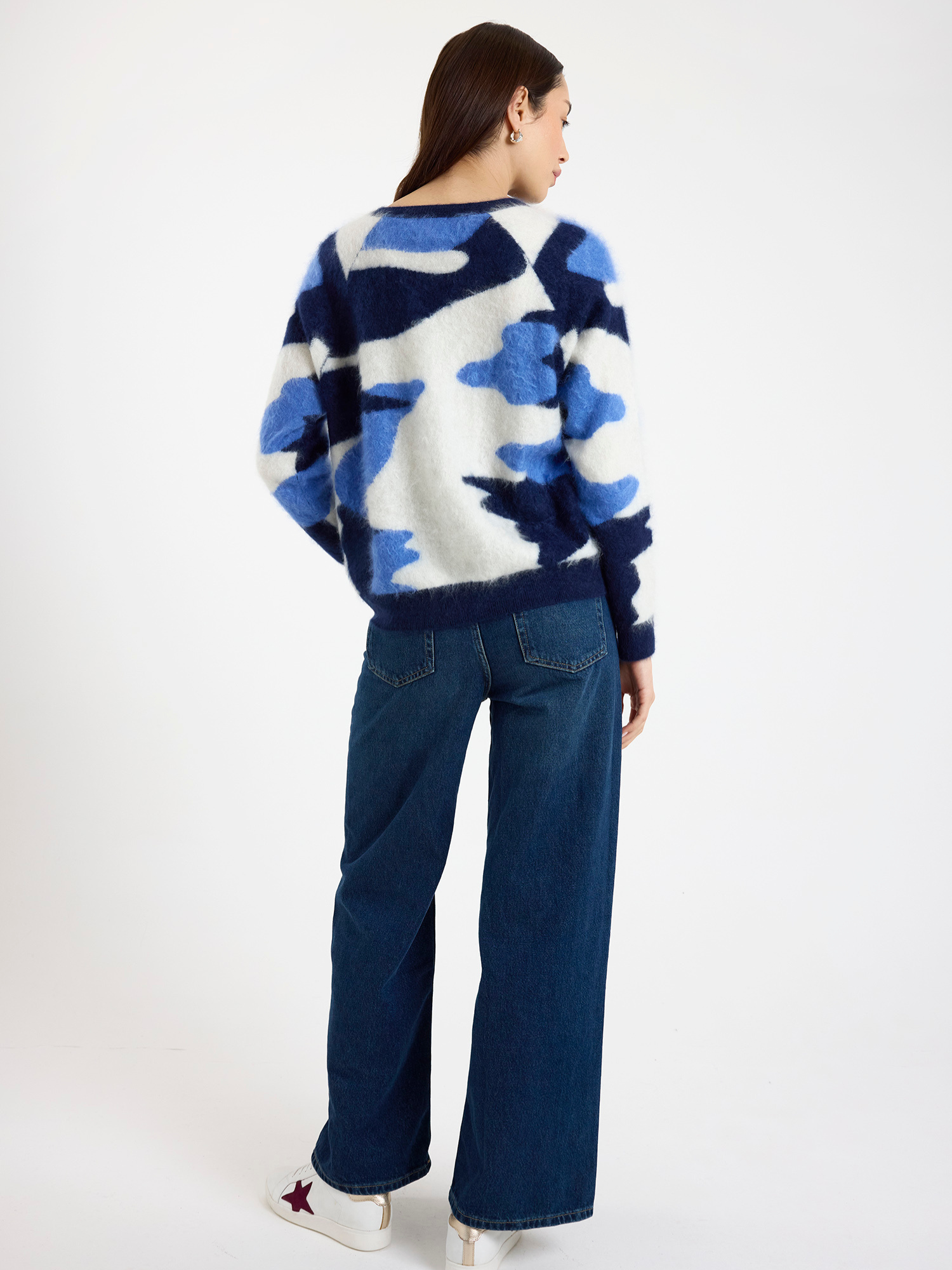 Woman wearing a blue and white camo patterned sweater and blue jeans on a white background