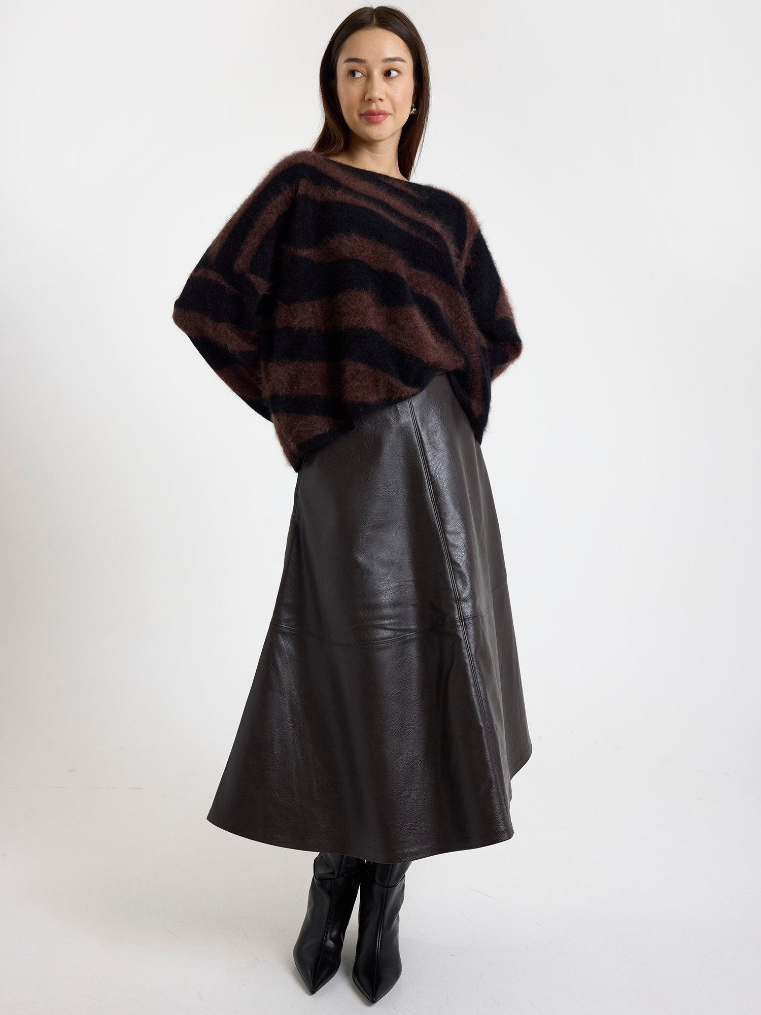 Woman wearing a brown and black zebra striped sweater with a brown leather skirt on a white background
