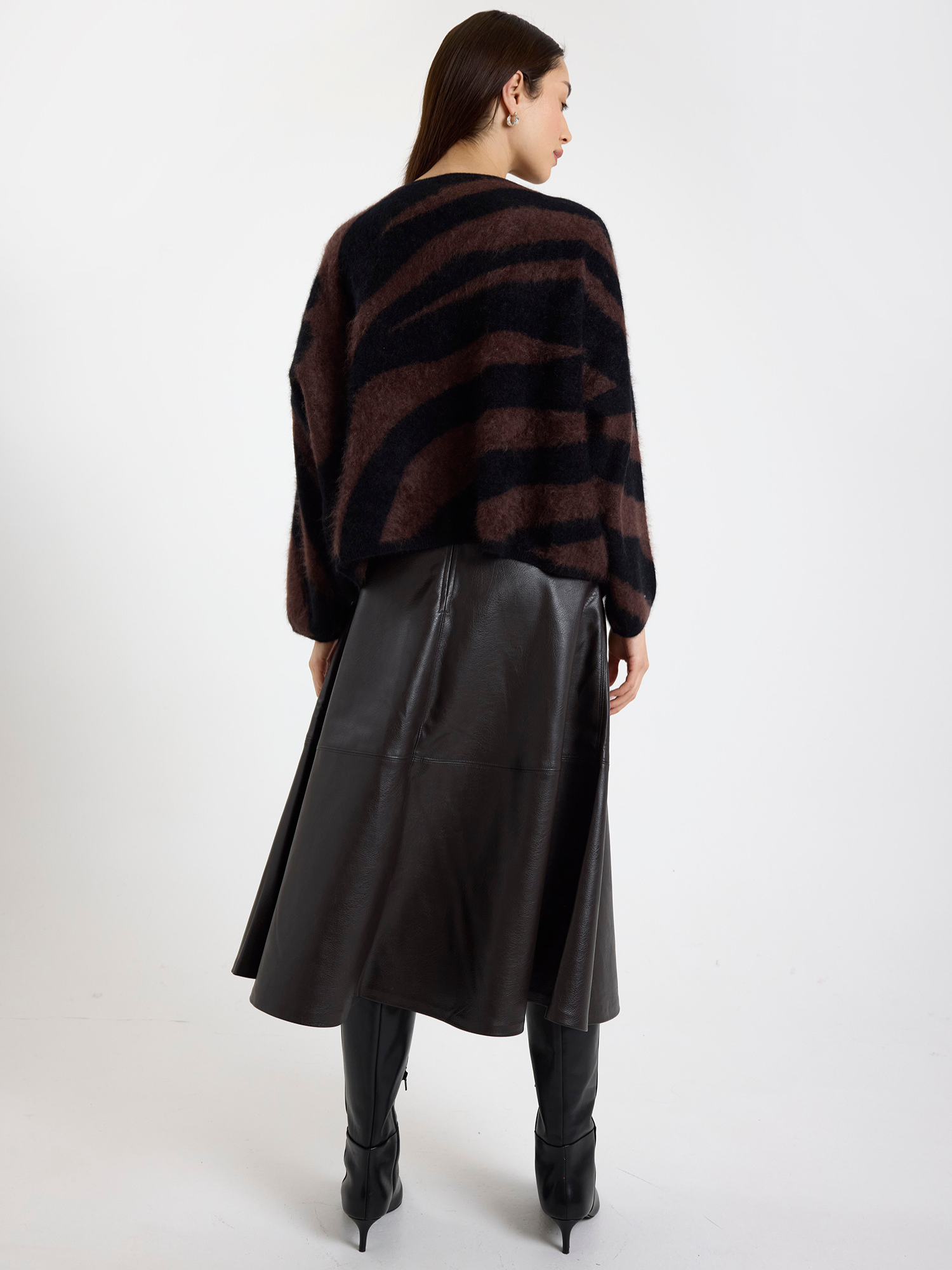 Woman wearing a brown and black zebra striped sweater with a brown leather skirt on a white background