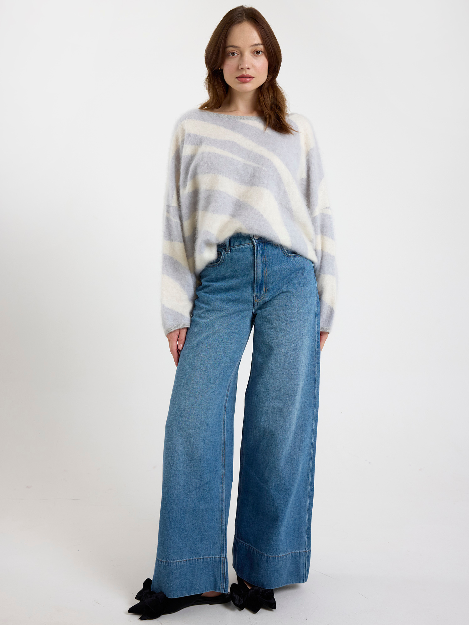 Woman wearing a grey and white zebra striped sweater and blue jeans on a white background