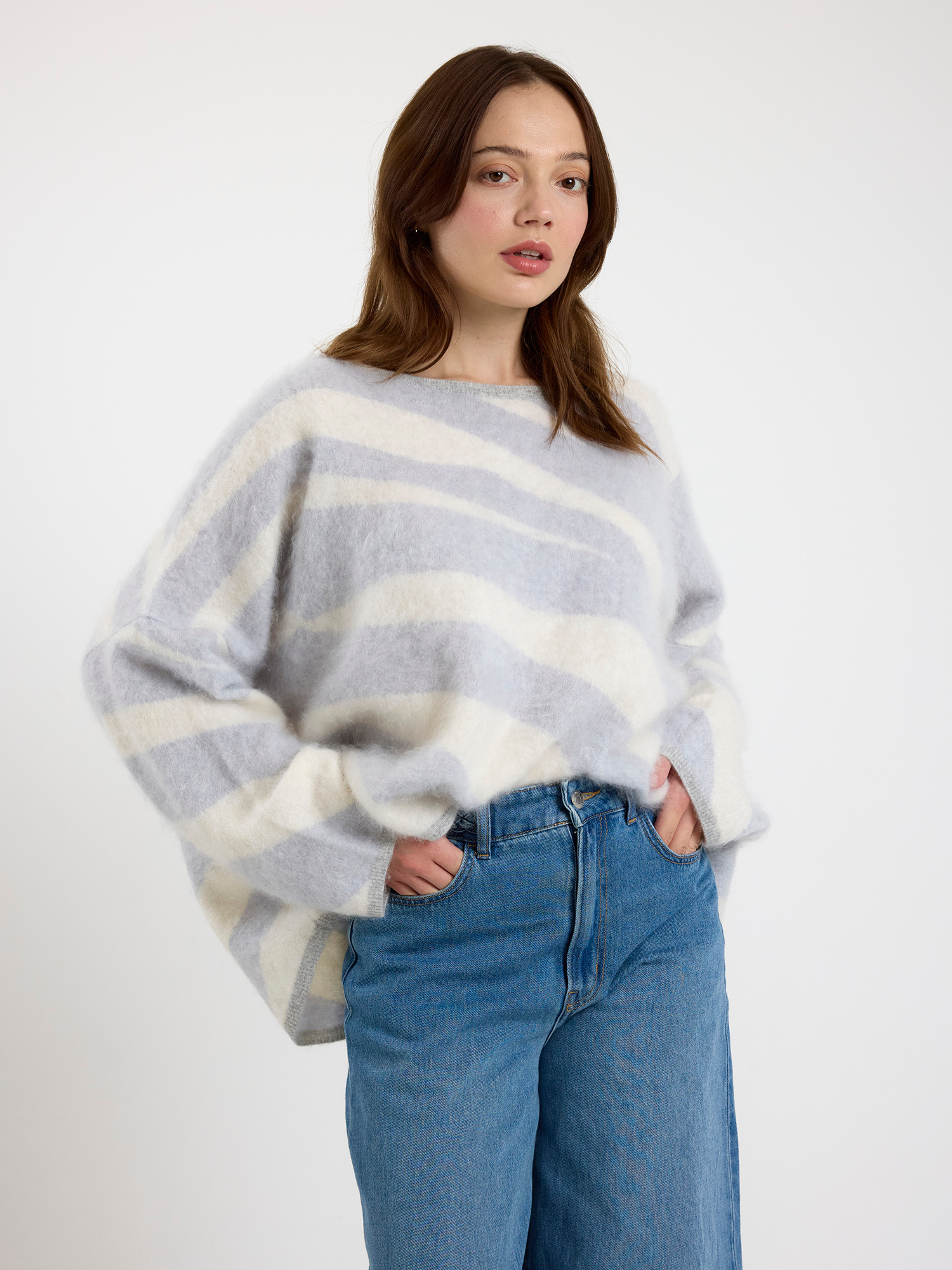 Woman wearing a grey and white zebra striped sweater and blue jeans on a white background