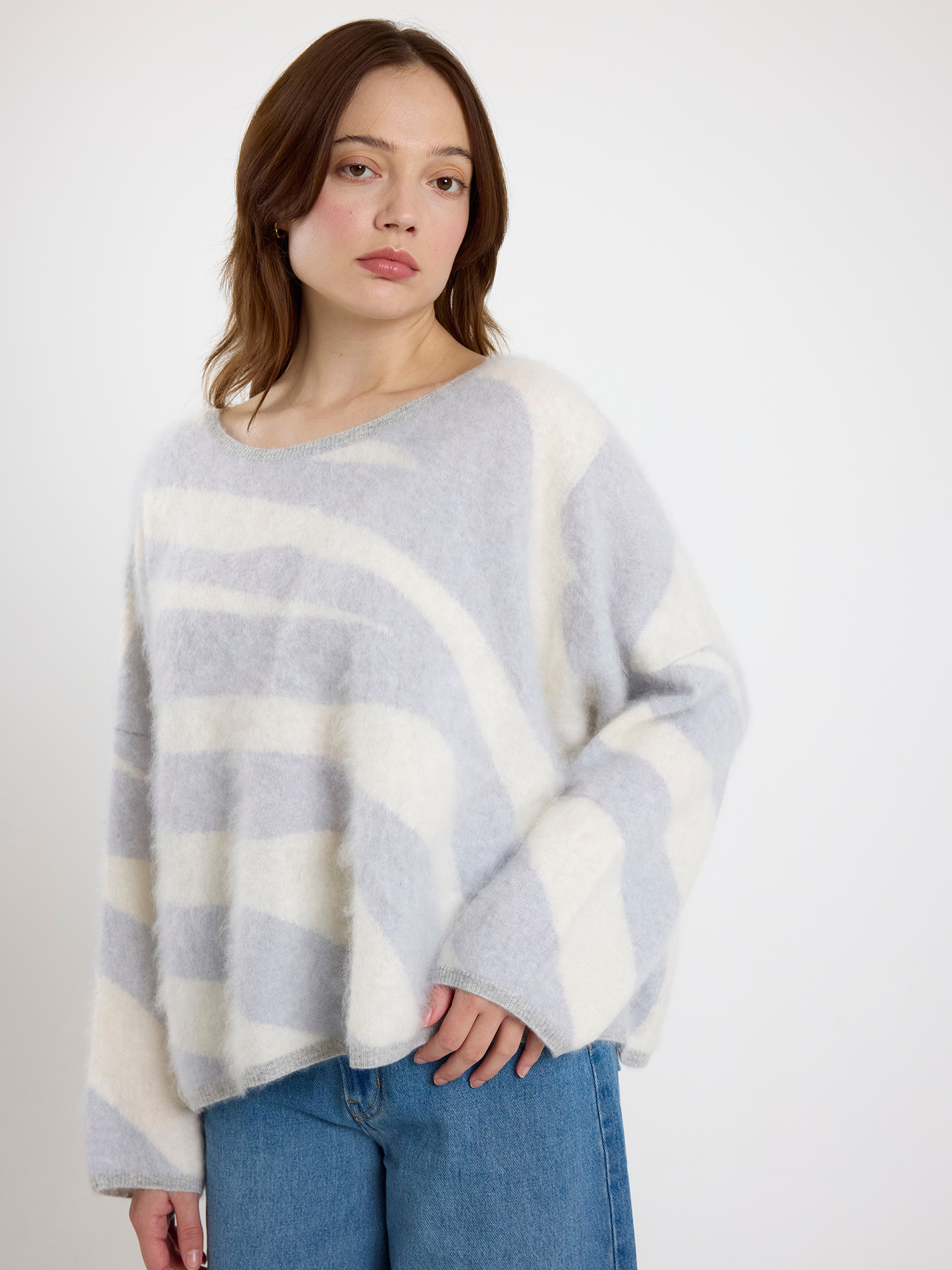 Woman wearing a grey and white zebra striped sweater and blue jeans on a white background