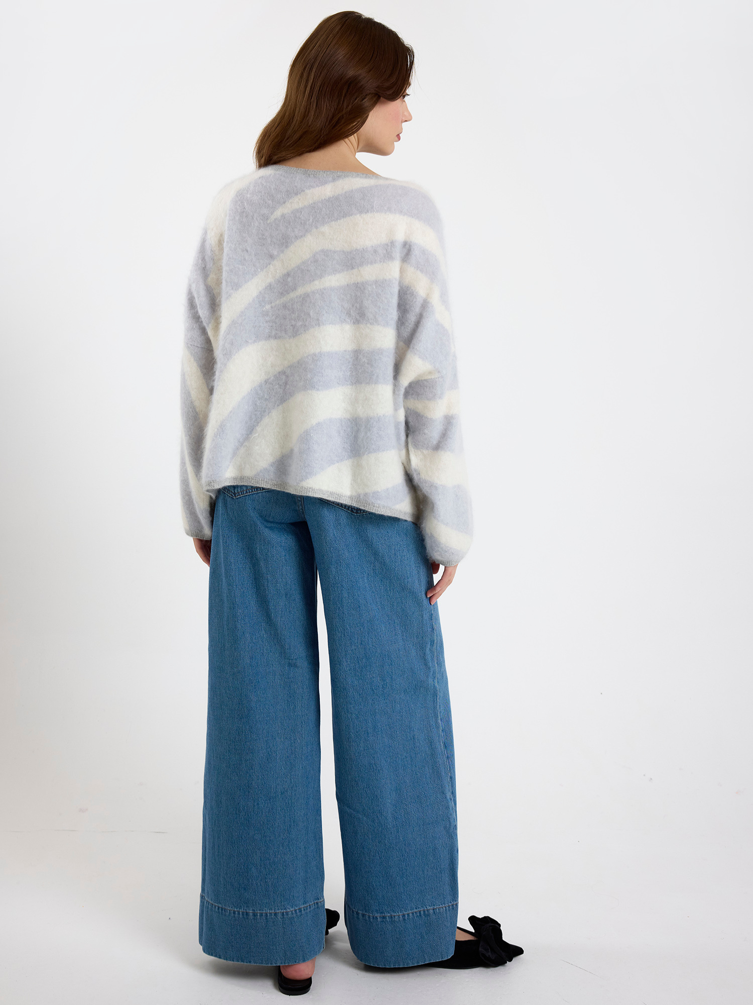Woman wearing a grey and white zebra striped sweater and blue jeans on a white background