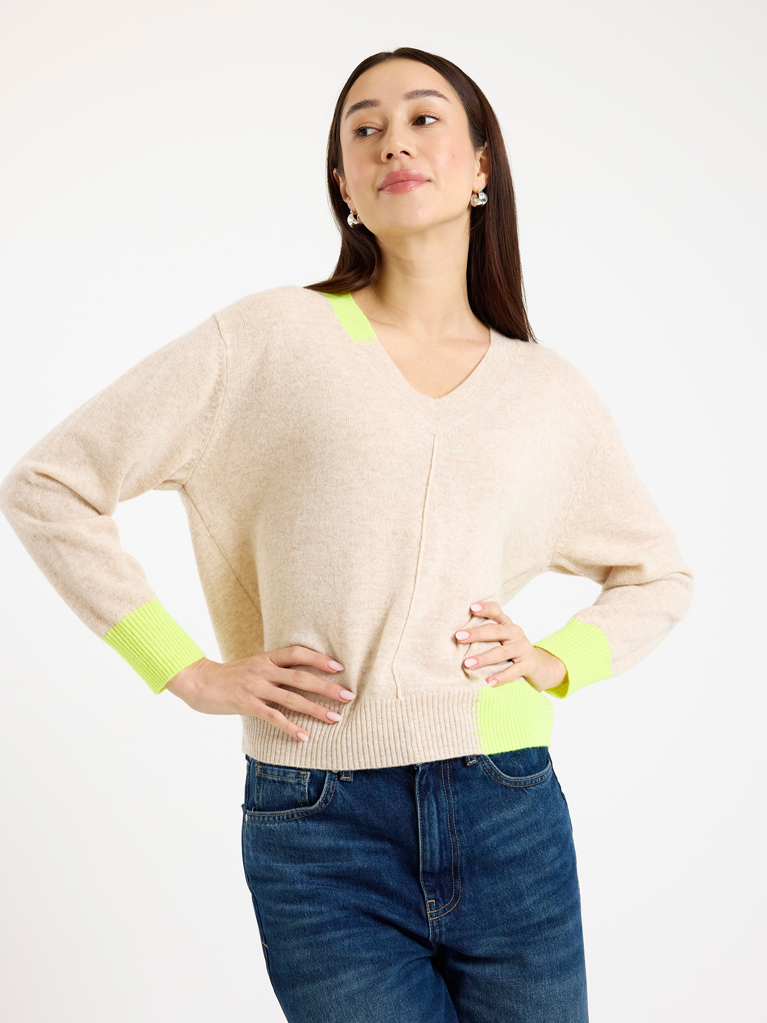 Woman wearing a beige sweater with neon yellow accents on a white background