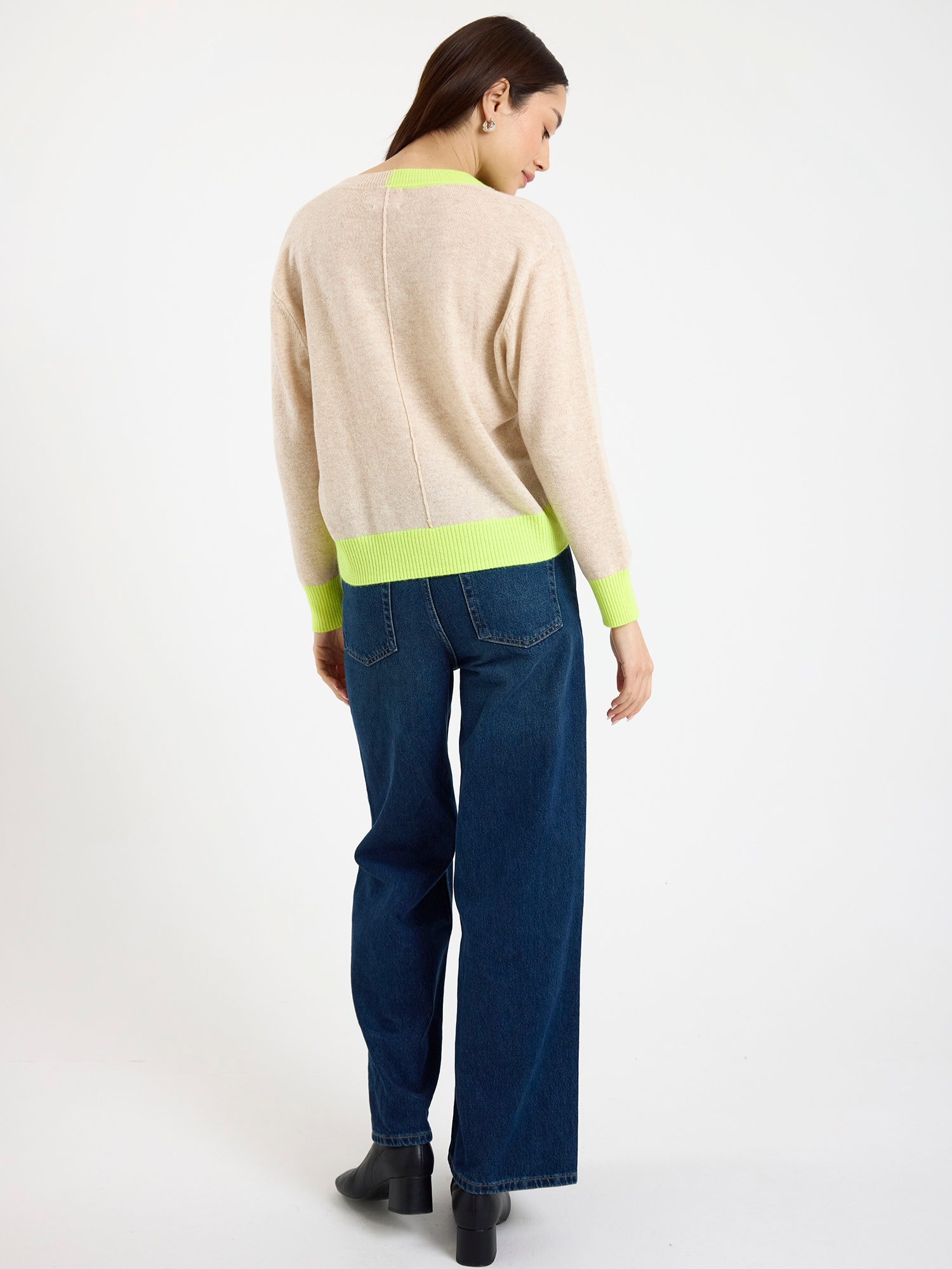 Woman wearing a beige sweater with yellow accents and blue jeans on a white background