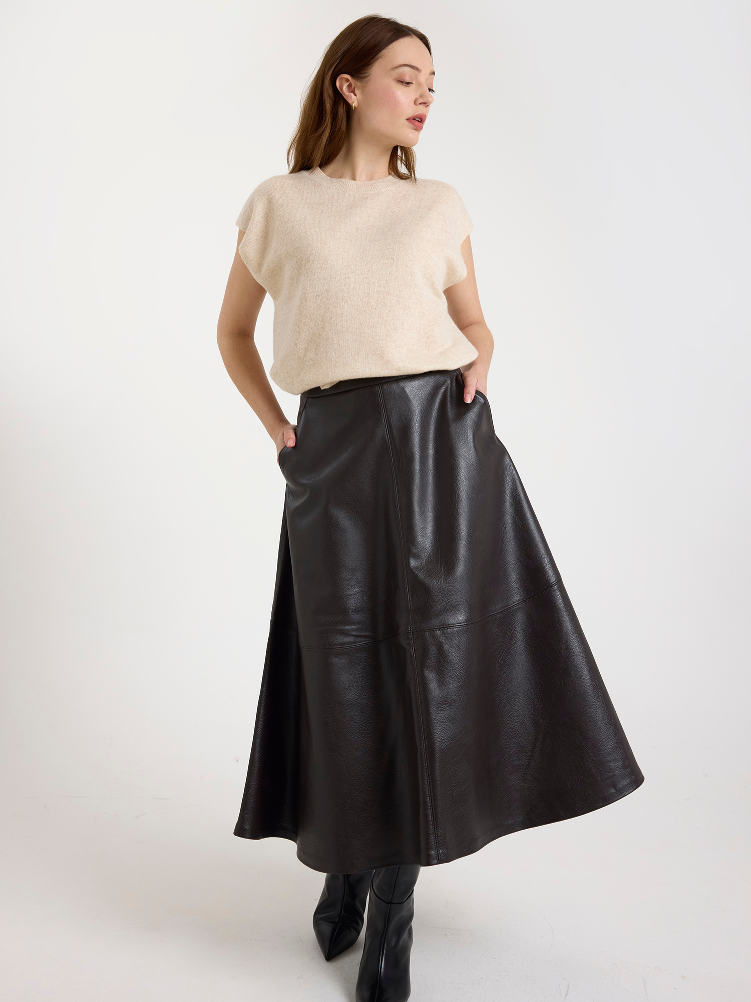 Woman wearing a sleeveless beige sweater and brown leather skirt on a white background