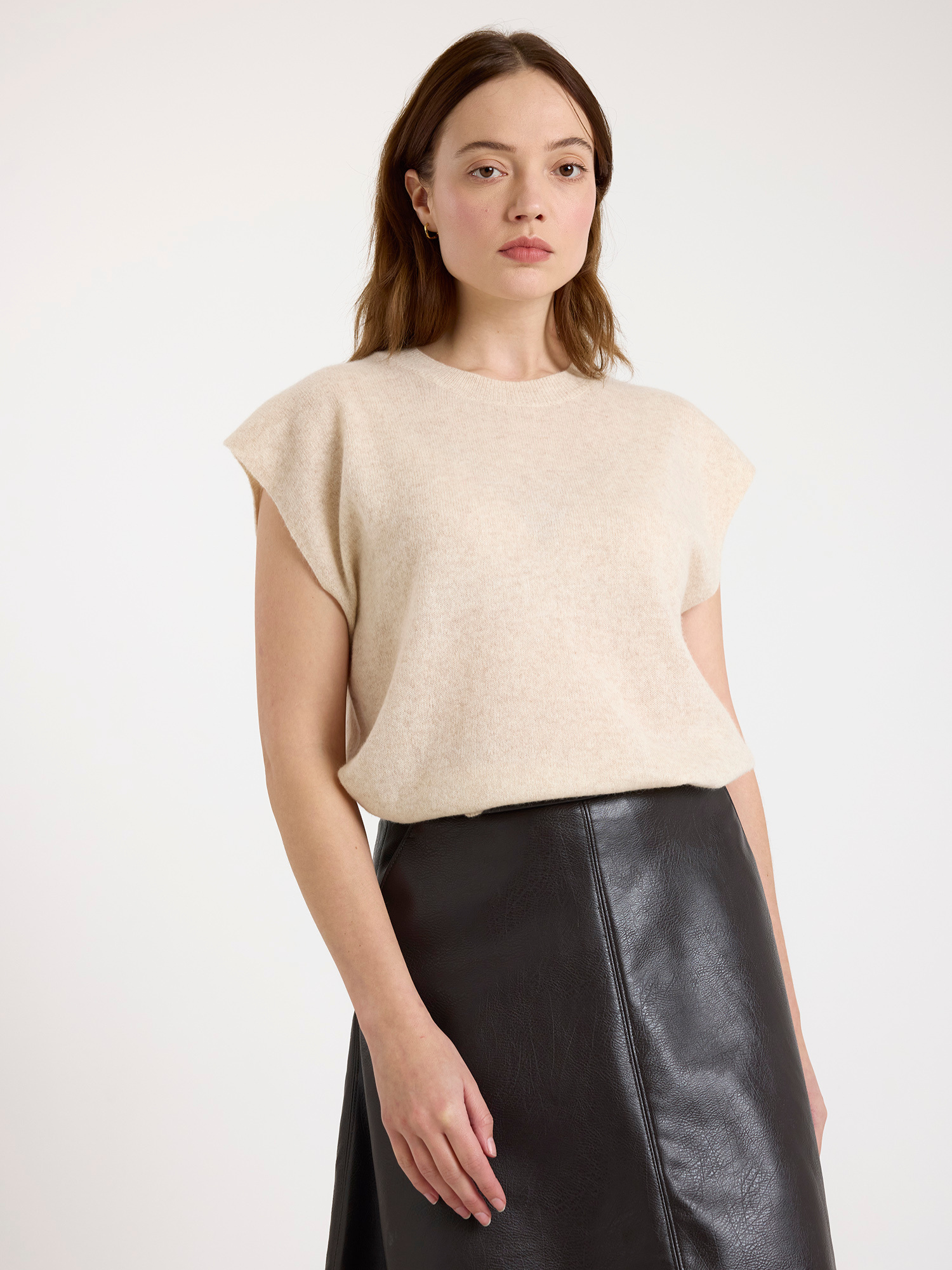 Woman wearing a sleeveless beige sweater and brown leather skirt on a white background