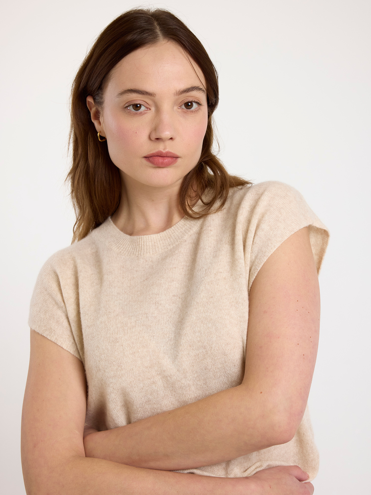 Woman wearing a beige sleeveless sweater against a white background