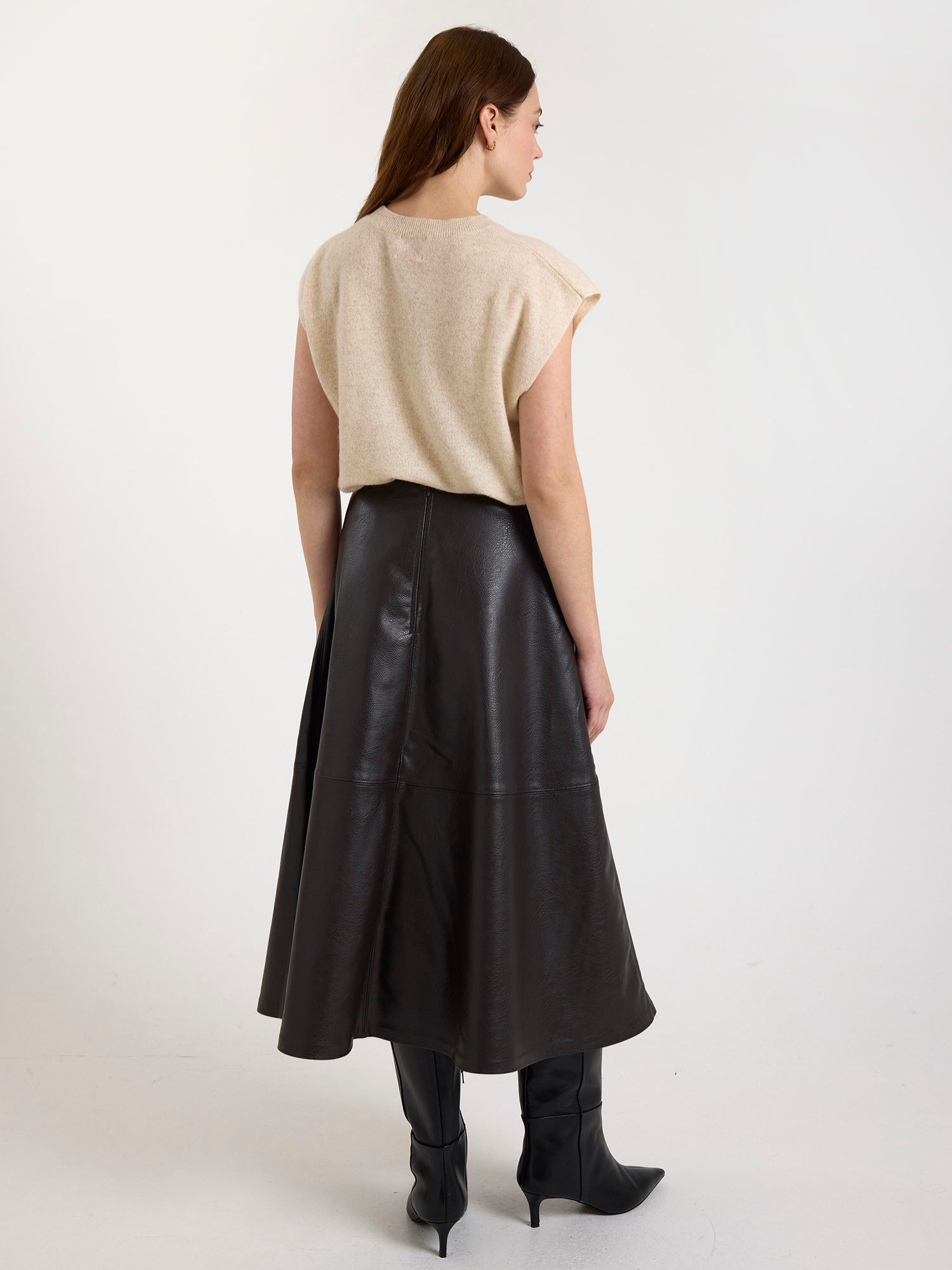 Woman wearing a sleeveless beige sweater and brown leather skirt on a white background