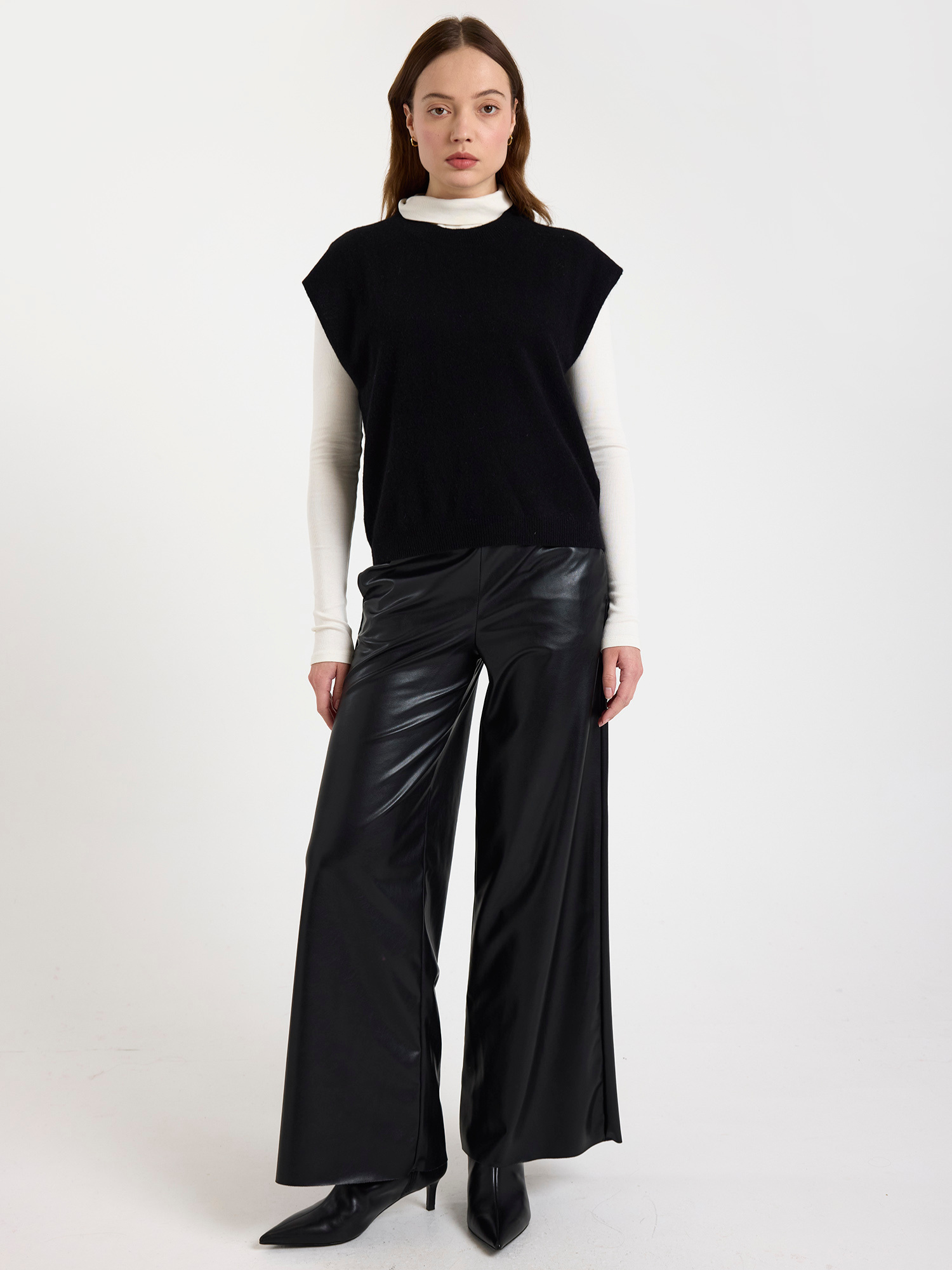 Woman wearing a black sleeveless top and black leather pants on a white background