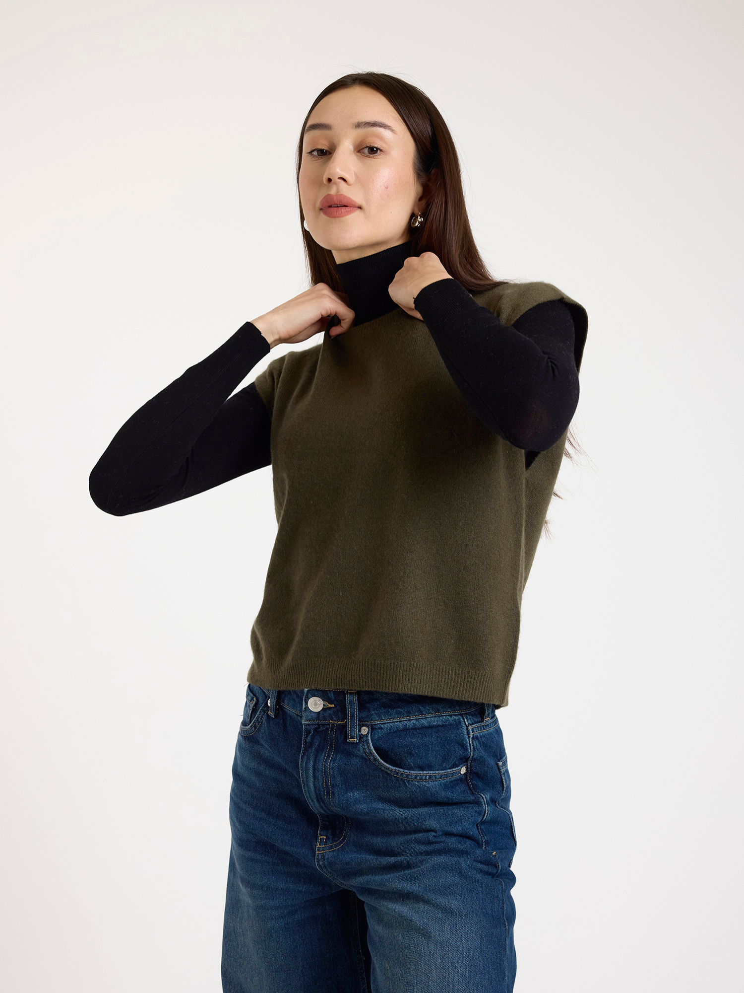 Woman wearing a green sleeveless sweater over a black turtleneck on a white background