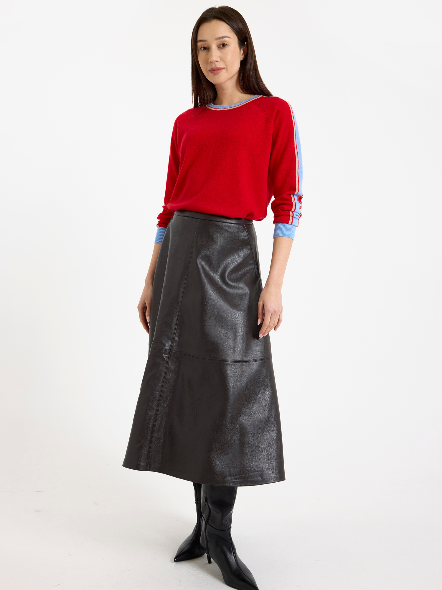 Woman wearing a red sweater with light blue stripes down the sleeve and brown leather skirt on a white background