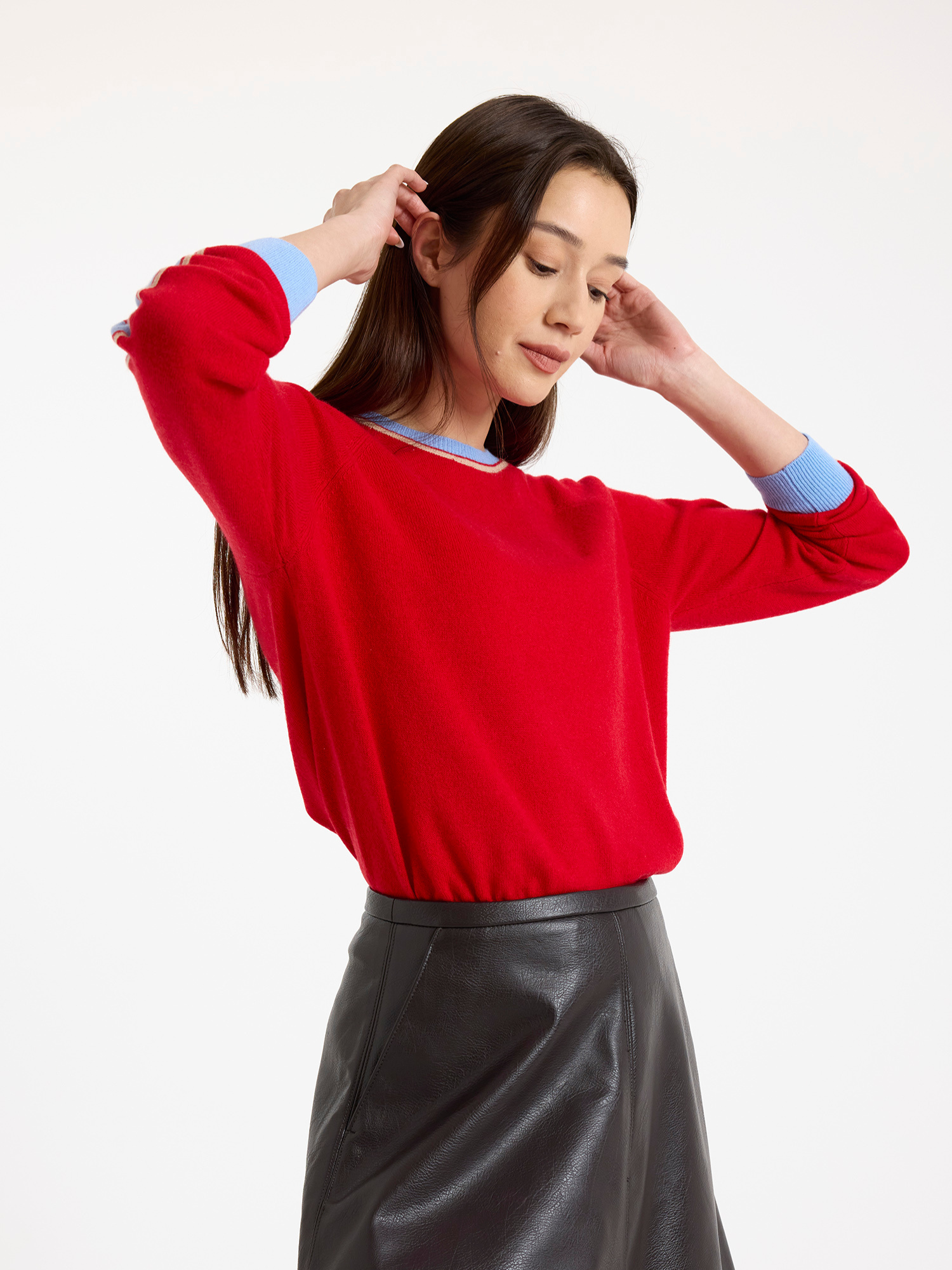 Woman wearing a red sweater with light blue stripes down the sleeve and brown leather skirt on a white background
