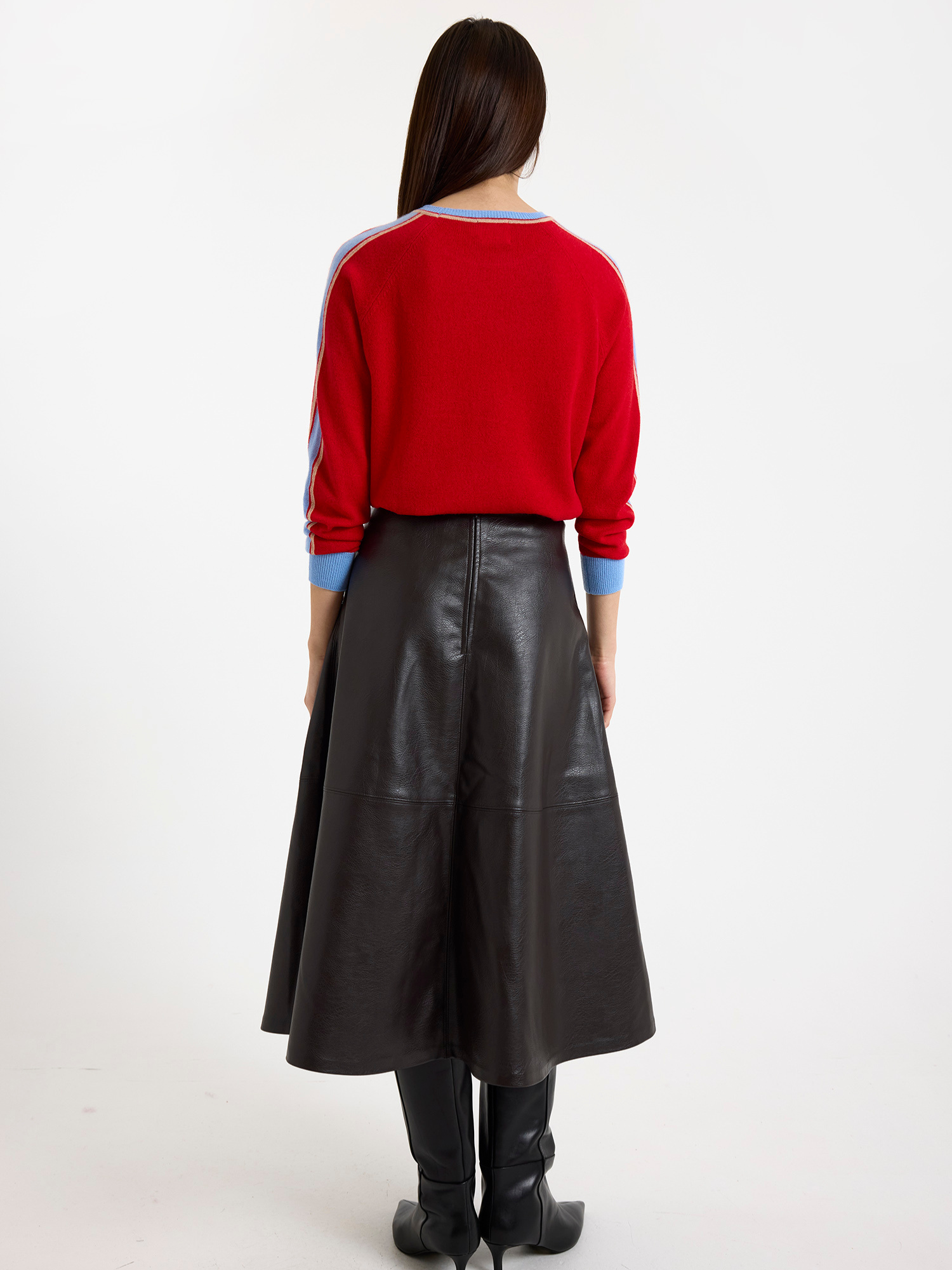 Woman wearing a red sweater with light blue stripes down the sleeve and brown leather skirt on a white background