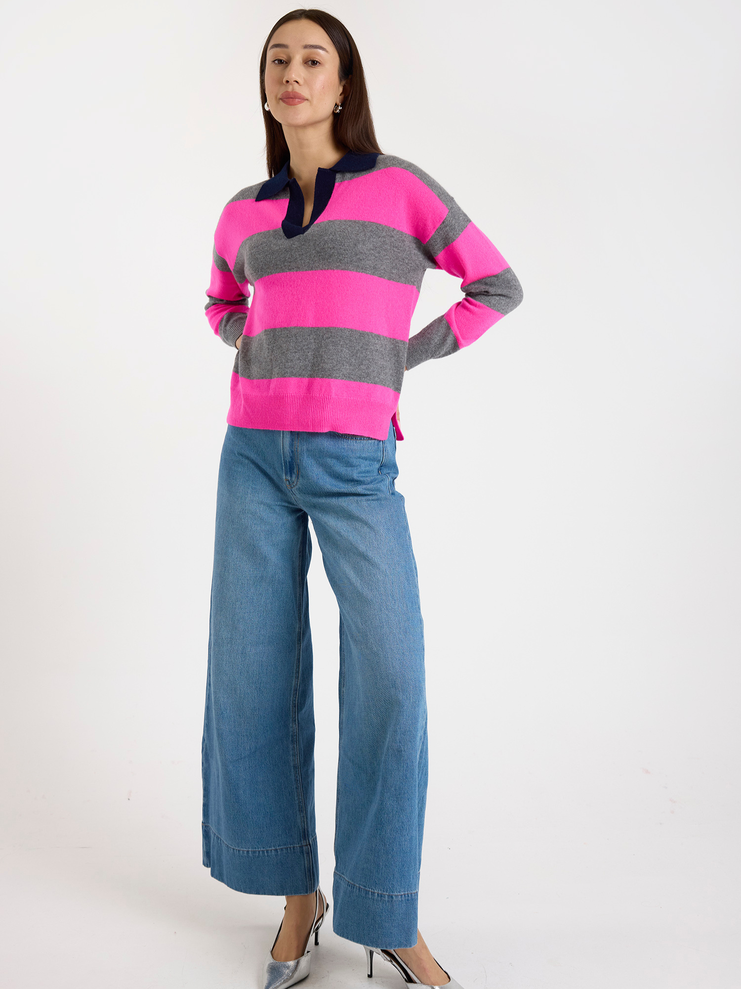 Woman wearing a pink and grey striped sweater with blue jeans on a white background