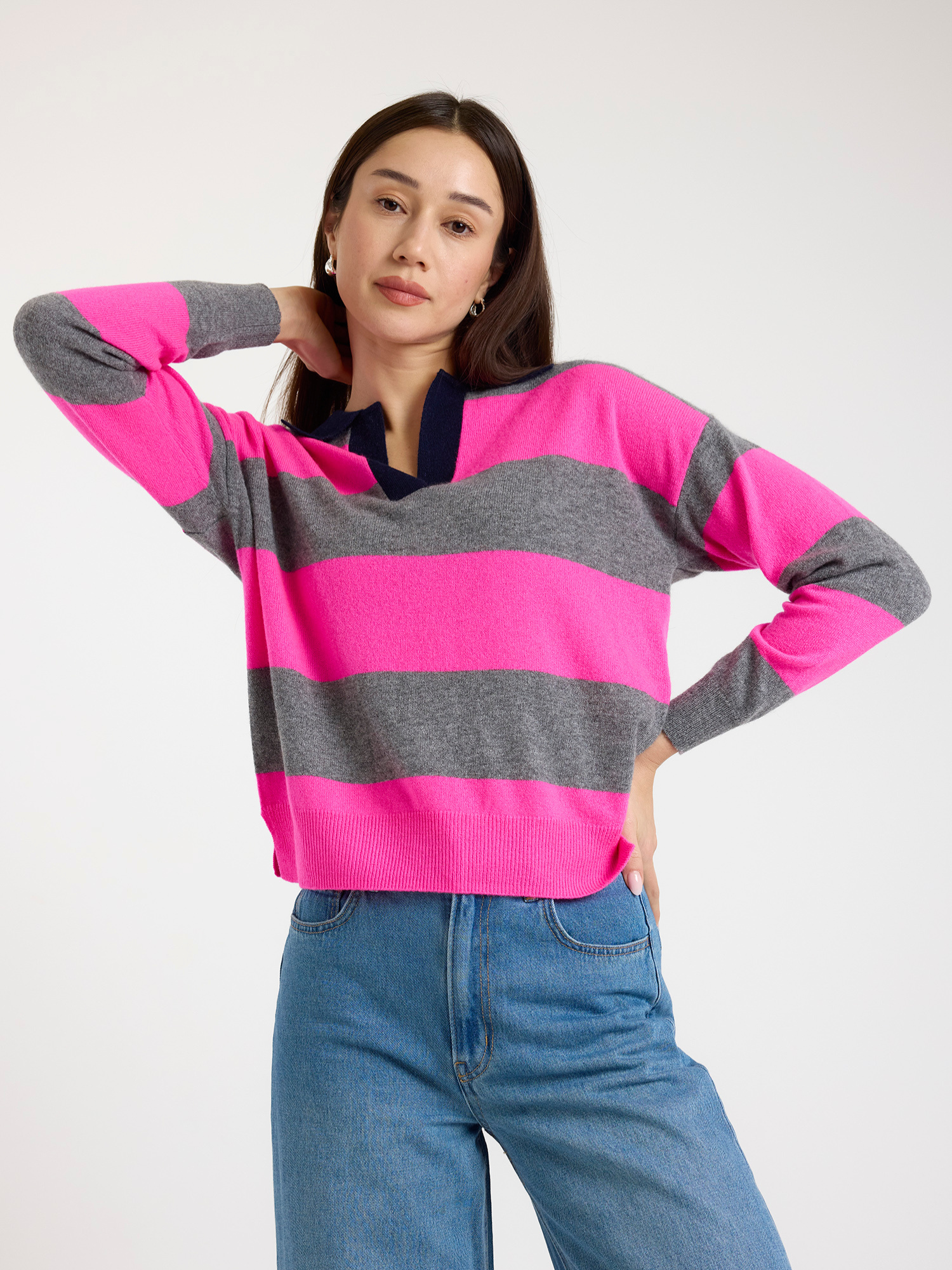 Woman wearing a pink and grey striped sweater with blue jeans on a white background