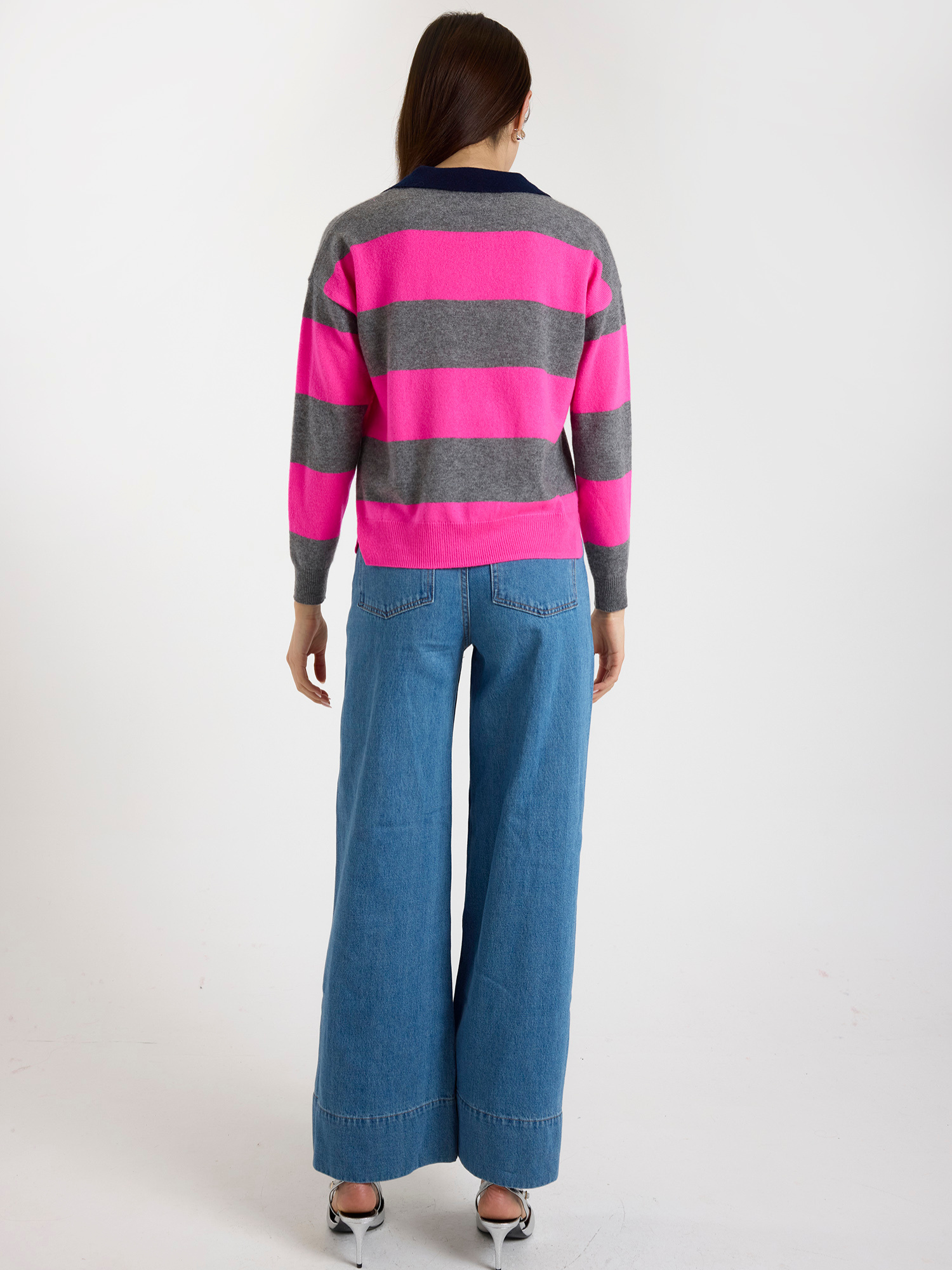Woman wearing a pink and grey striped sweater and blue jeans on a white background
