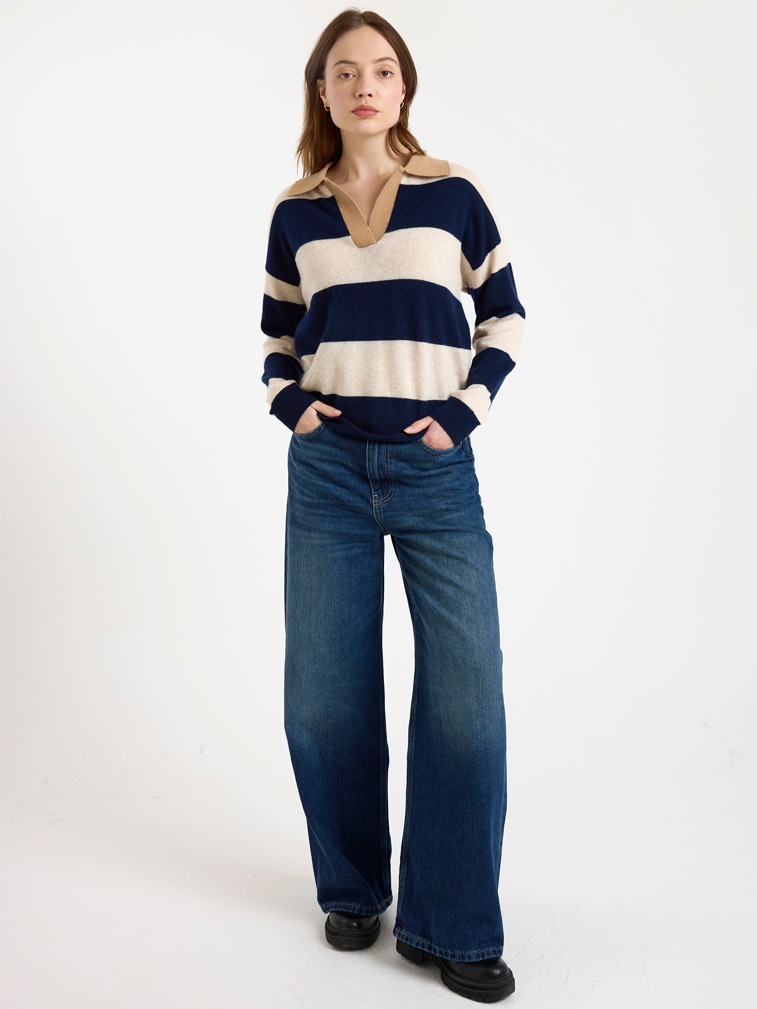Woman wearing a navy and beige striped sweater with blue jeans on a white background