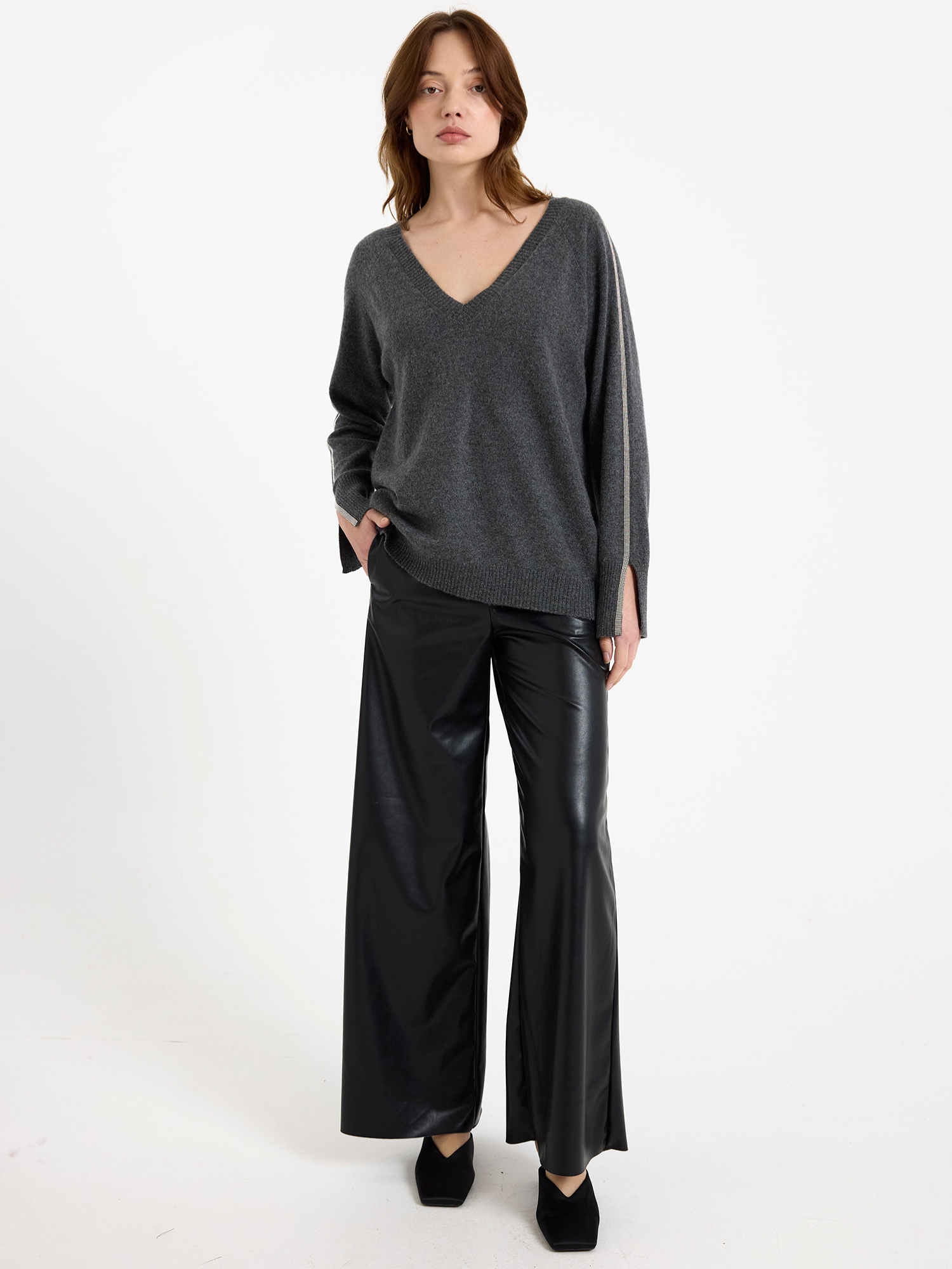 Woman wearing a grey sweater with glitz detail down the arm and black wide-leg pants on a white background
