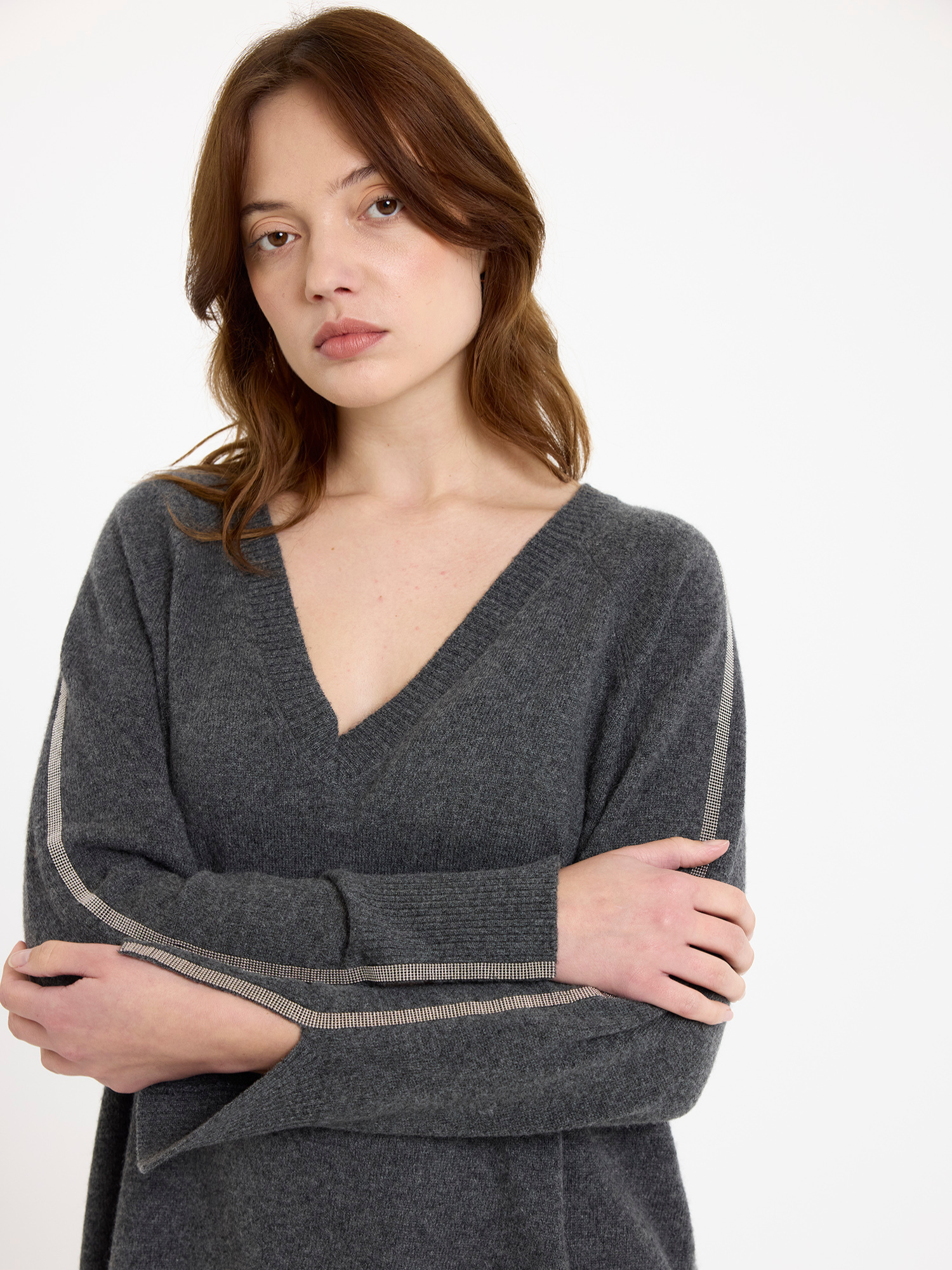 Woman wearing a grey sweater with glitz detail down the arm on a white background