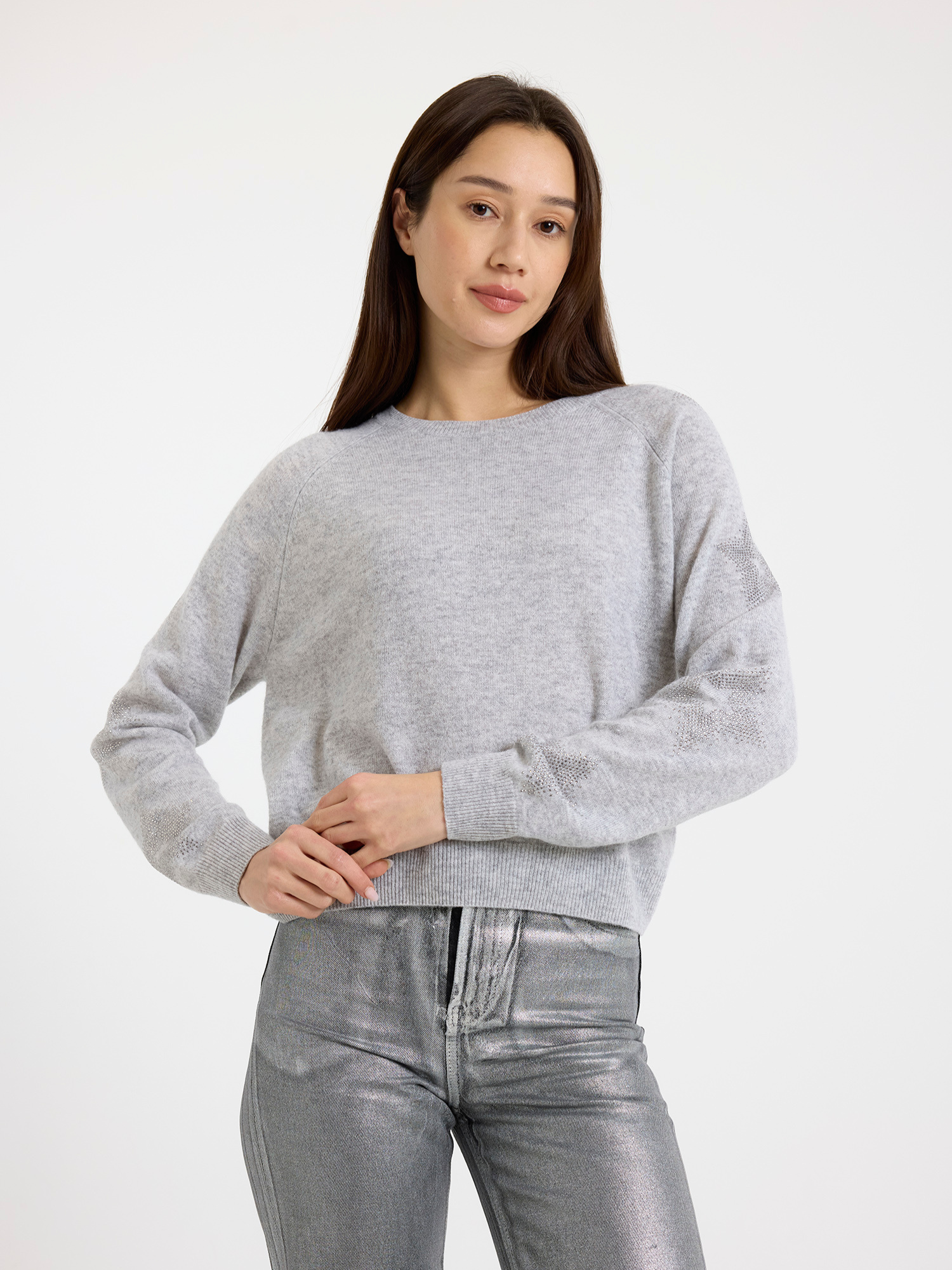 Woman wearing a grey sweater with star detail and silver jeans on a white background