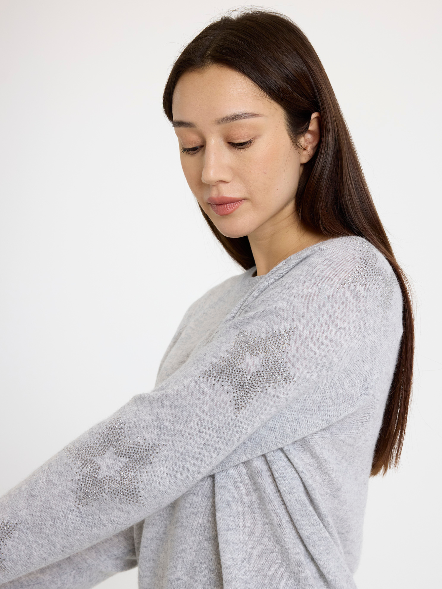 Woman wearing a grey sweater with subtle star design and silver pants on a white background