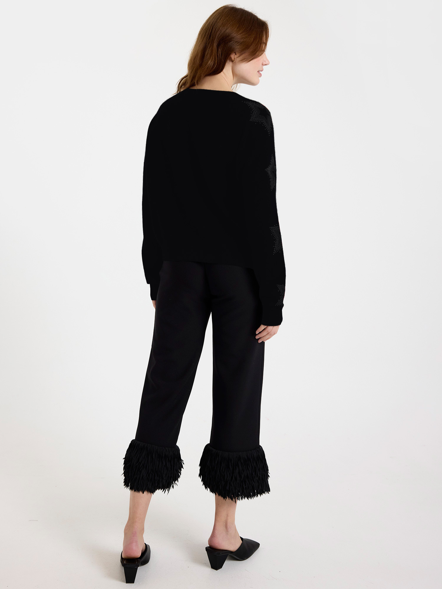 Woman wearing a black sweater with subtle star design on the sleeves with ruffled pants on a white background