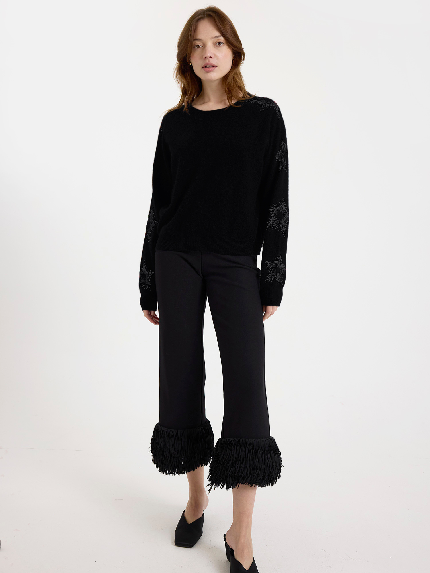 Woman wearing a black sweater with subtle star design on the sleeves with ruffled pants on a white background