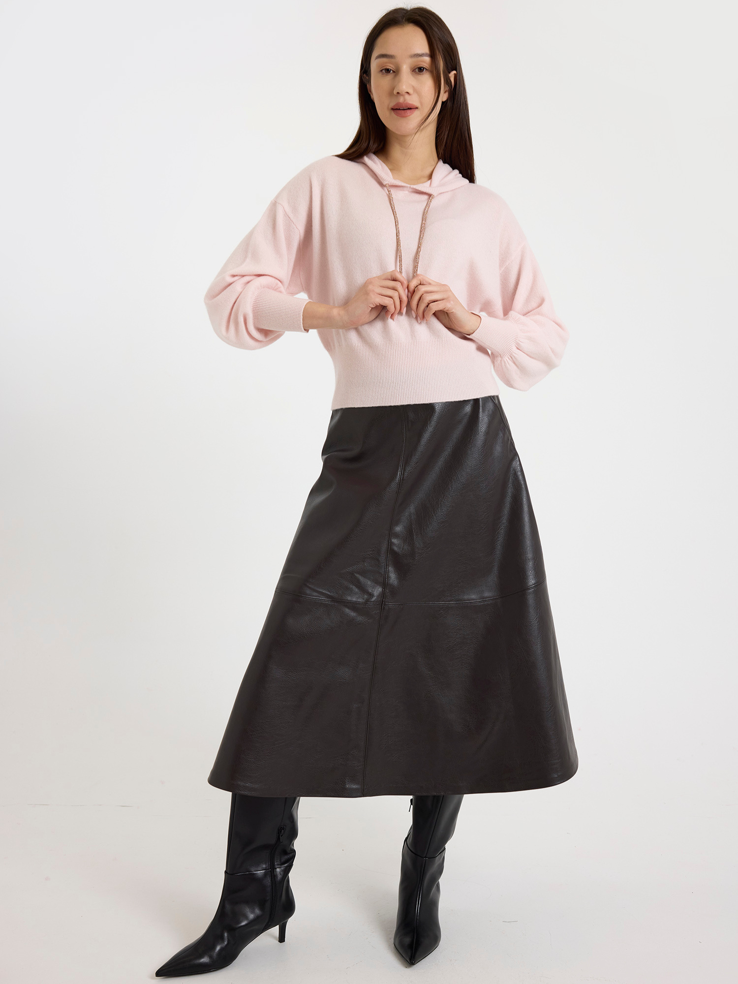 Woman wearing a light pink hoodie and brown leather skirt on a white background