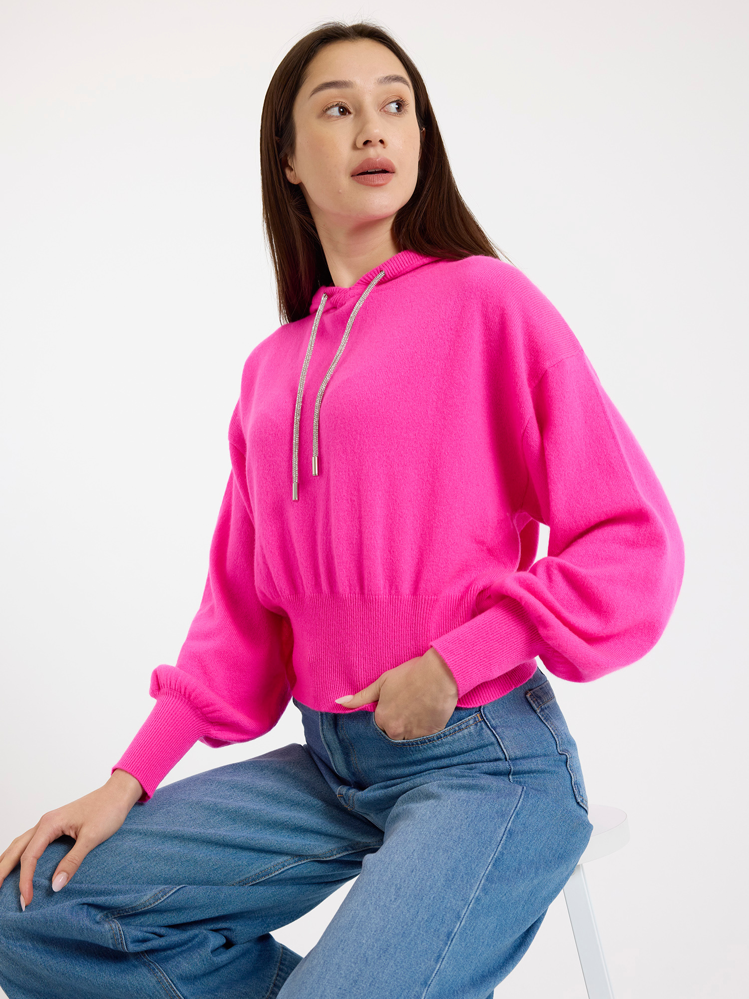 Woman wearing a bright pink hoodie and blue jeans on a white background