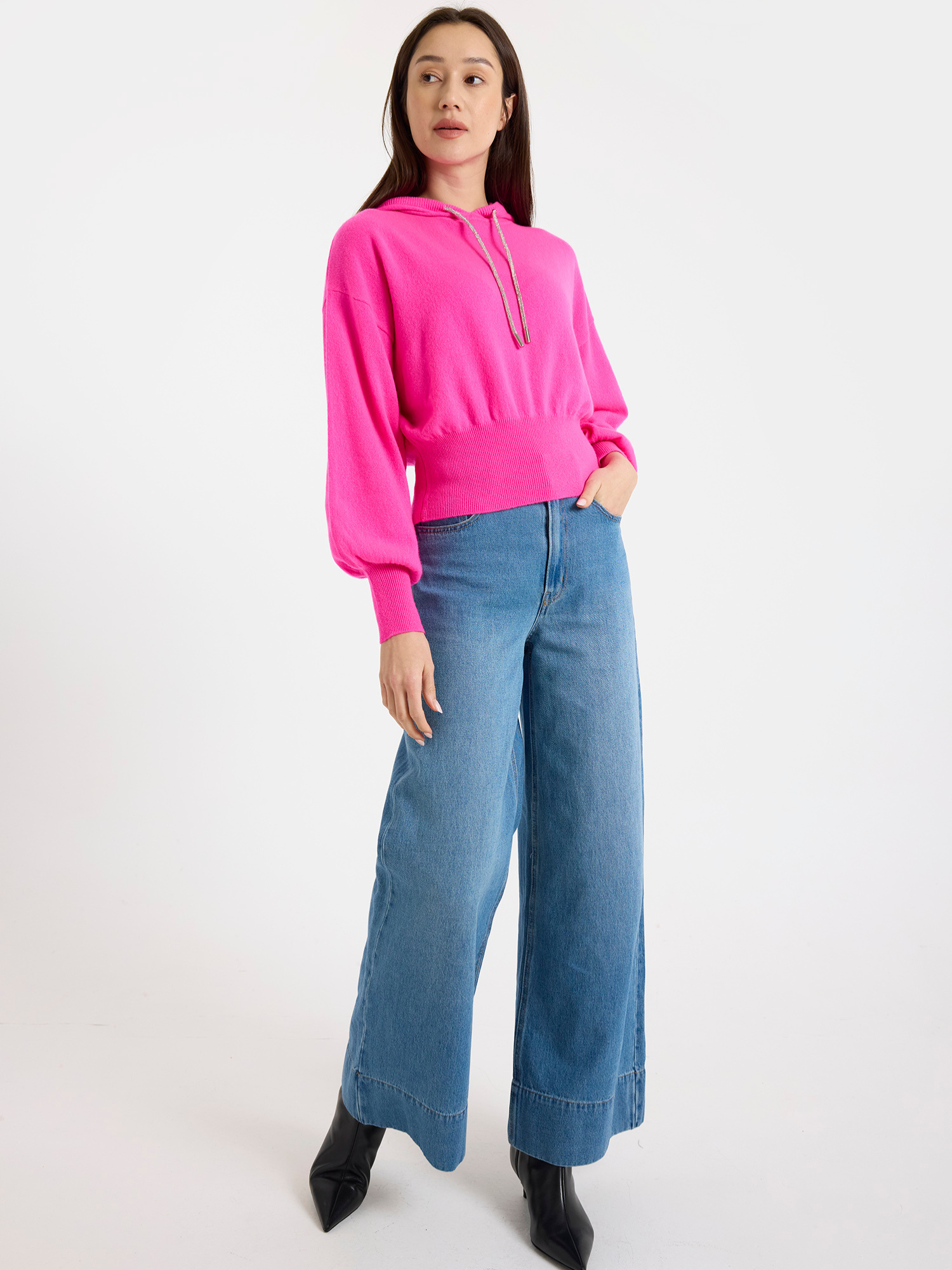 Woman wearing a bright pink hoodie and blue jeans on a white background