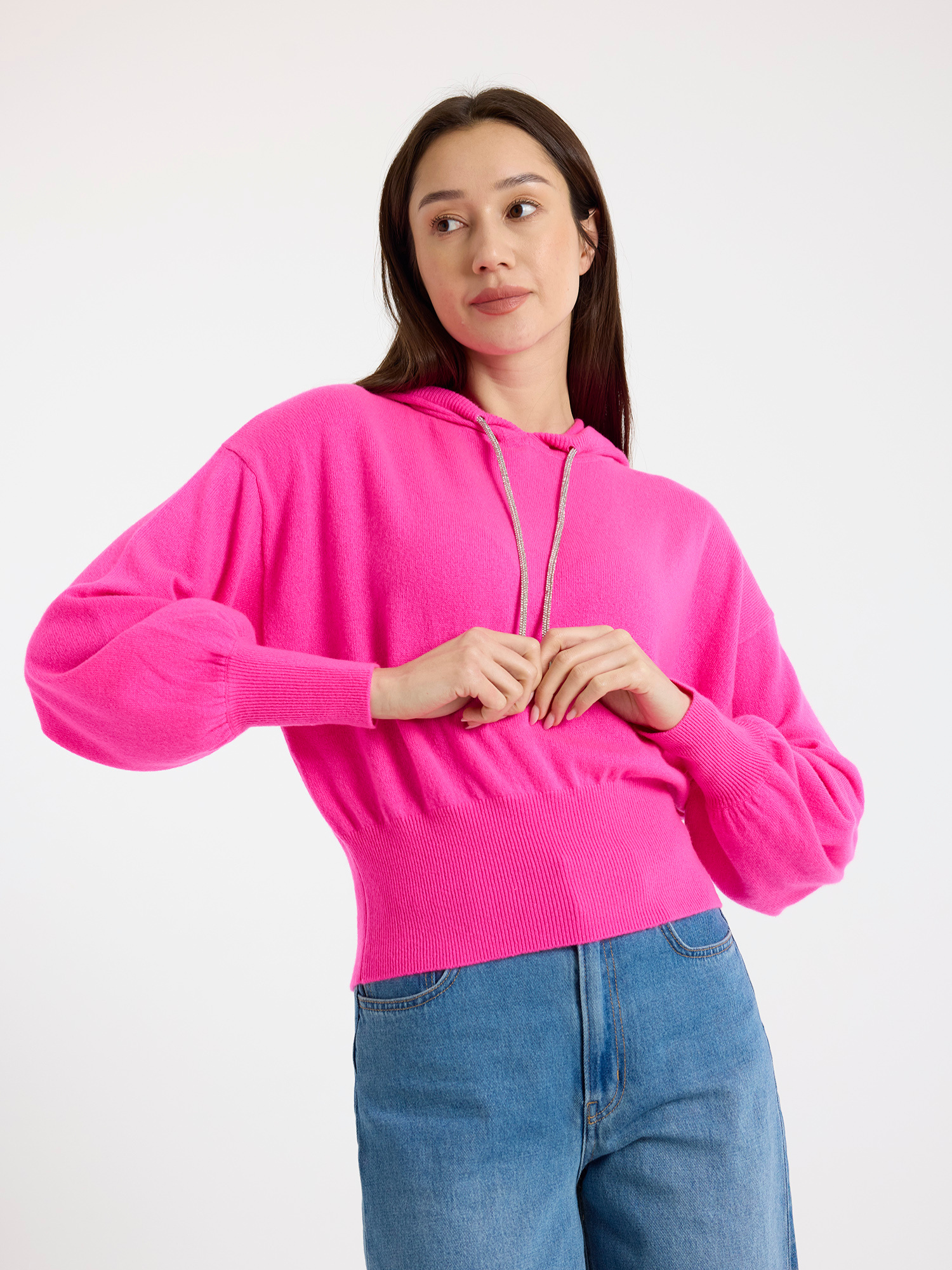 Woman wearing a bright pink hoodie and blue jeans on a white background